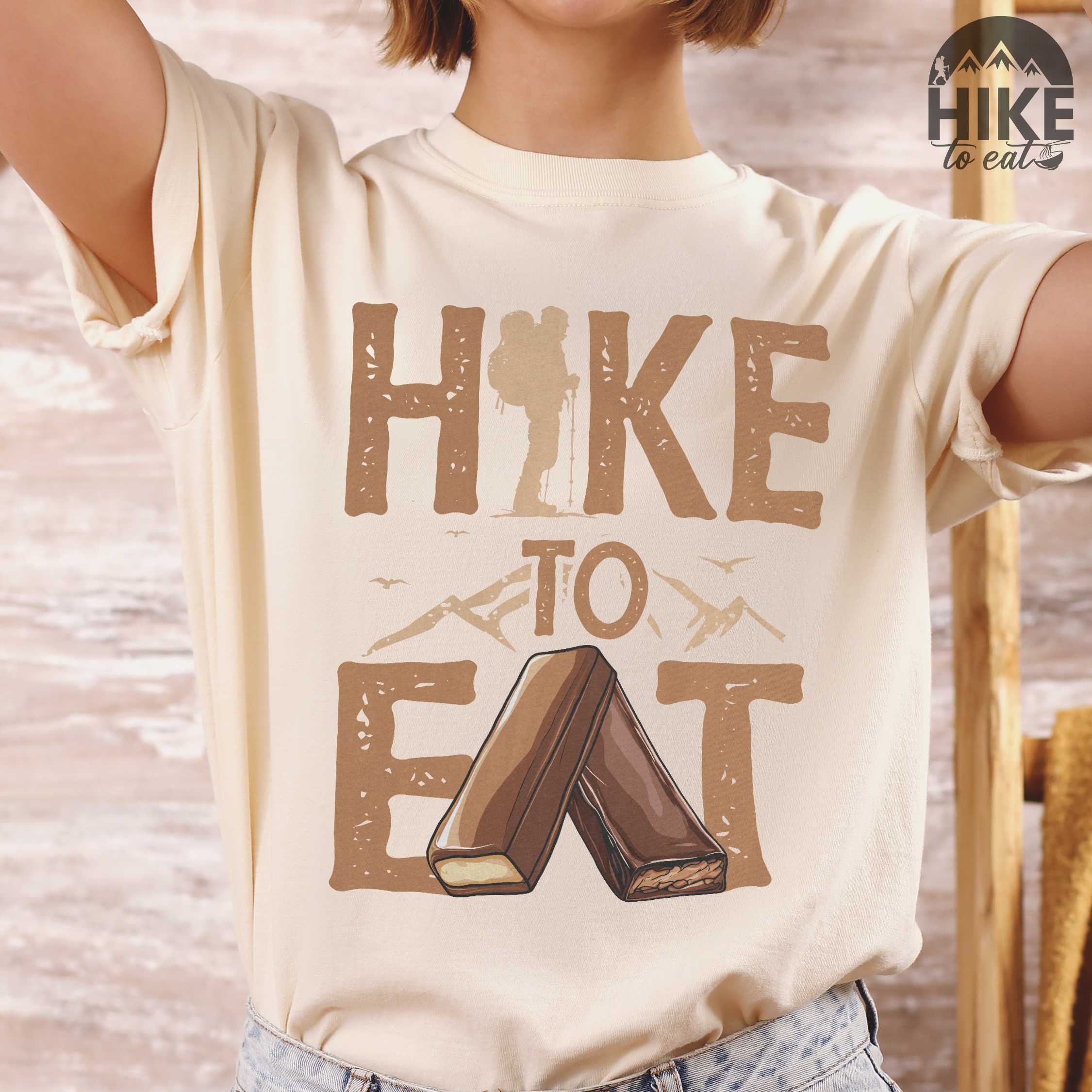 Woman wearing ivory "Hike to Eat" colored statement tee with bold typography, mountain, illustrated bars of chocolate, perfect for chocolate lovers.