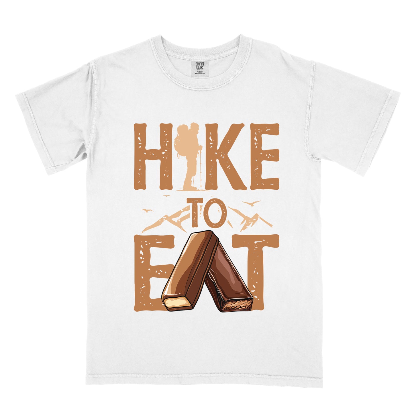 White t-shirt with tan/brown distressed text reading "HIKE TO EAT". "HIKE" appears in large brown letters at the top with a hiker silhouette integrated into the letter "I", "TO" in brown text with small mountain outlines on either side in the middle, and "EAT" in large brown letters at the bottom with two chocolate candy bars arranged in an "A" shape replacing the letter "A". Small flying birds appear near "TO".