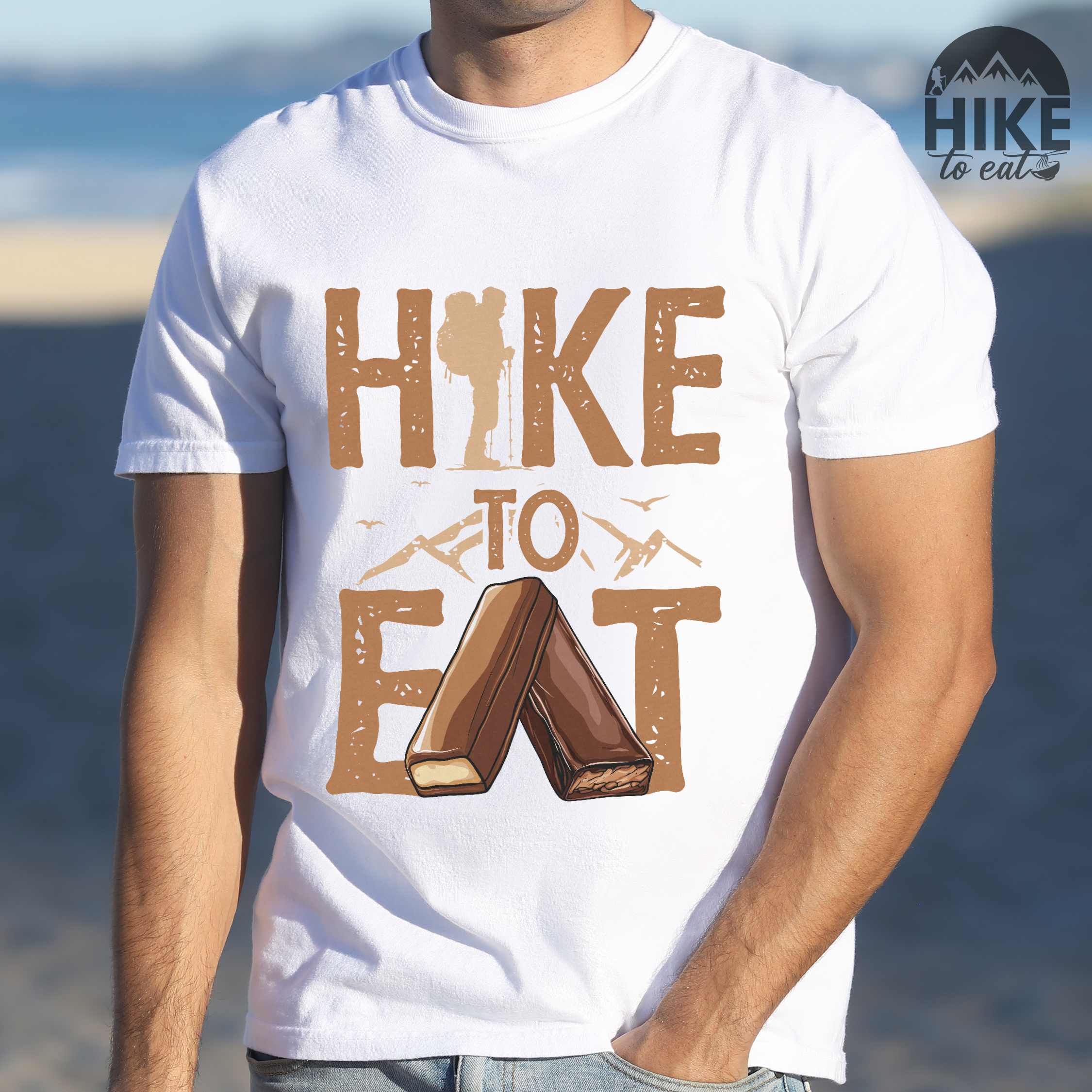 Man wearing white "Hike to Eat" colored statement tee with bold typography, mountain, illustrated bars of chocolate, perfect for chocolate lovers.