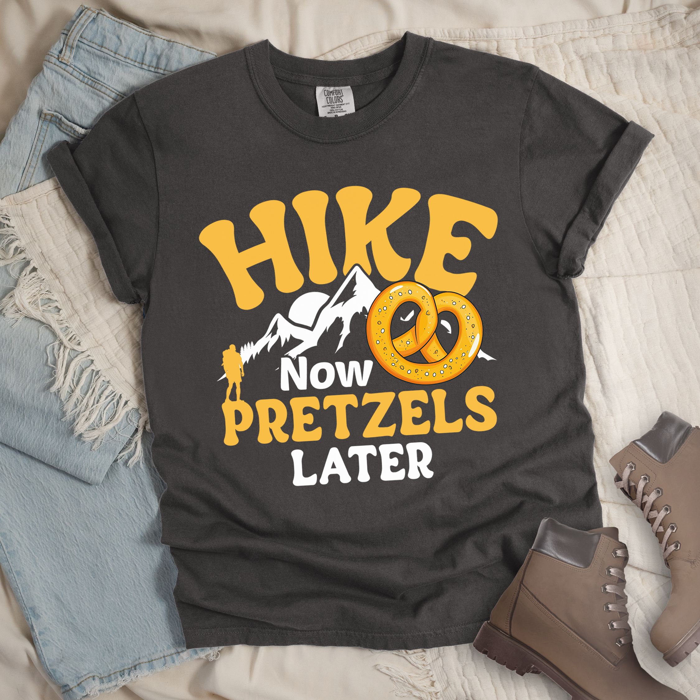 Dark grey shirt with “Hike Now Pretzels Later” in yellow and white text, featuring a hiker silhouette, mountain outline, and two golden pretzels.