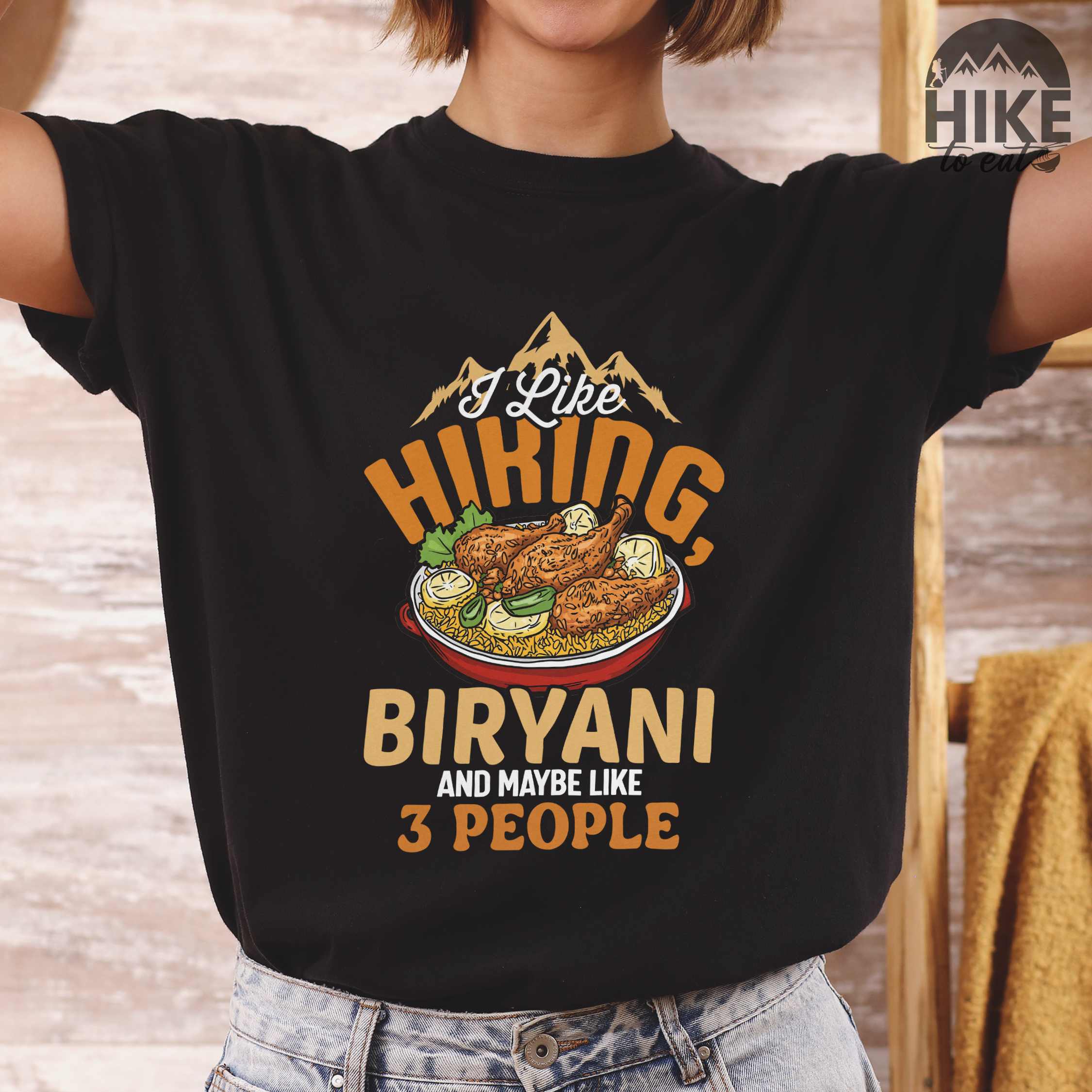 woman wearing black “I Like Hiking, Biryani and Maybe Like 3 People” colored vintage tee with bold text, featuring a steaming bowl of biryani with chicken, lemon wedges, and herbs. Perfect tee for biryani rice lovers.