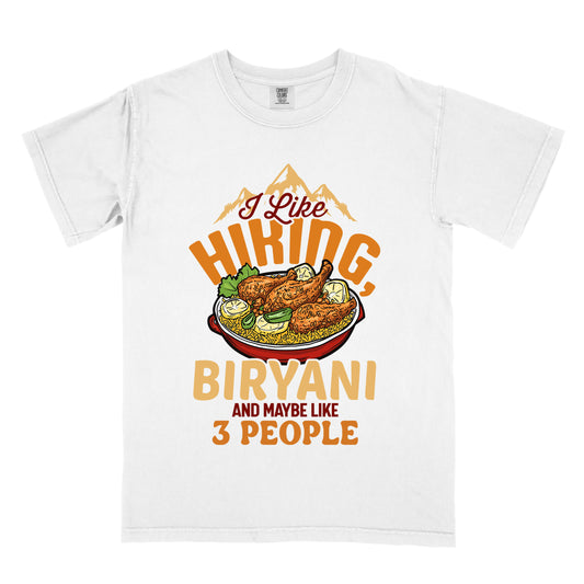 White t-shirt with text reading "I Like HIKING, BIRYANI AND MAYBE LIKE 3 PEOPLE". Gold mountain silhouettes appear above "I Like" (in dark brown script). "HIKING" is in large orange letters, below which sits a detailed illustration of a red bowl filled with biryani rice and chicken. "BIRYANI" appears in gold letters, while "AND MAYBE LIKE" is in small dark brown text and "3 PEOPLE" in orange.