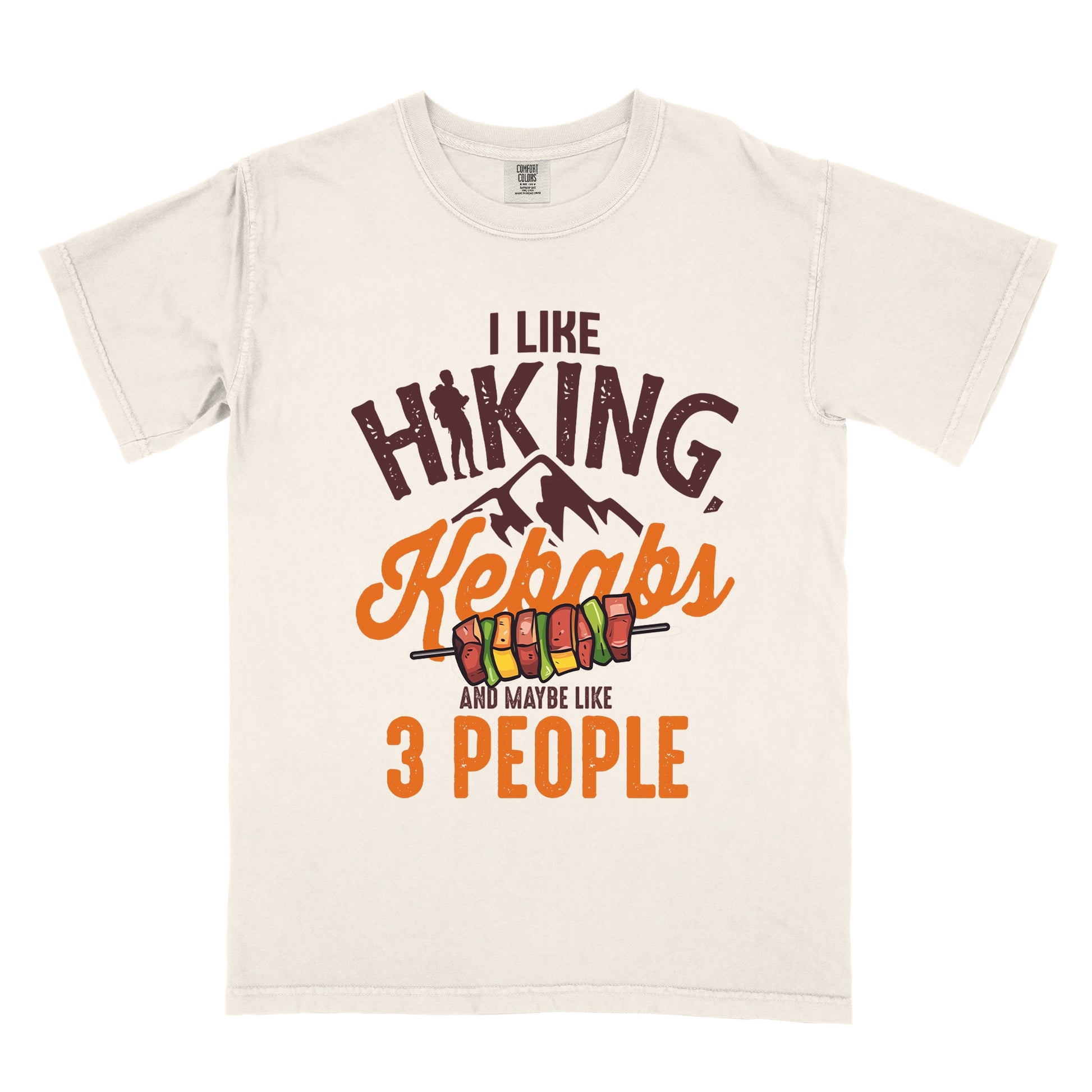Ivory (Cream White) t-shirt with dark brown text "I LIKE HIKING," with the letter "I" in "HIKING" replaced by a hiker silhouette. Below that is "Kebabs" in orange script with an illustration of a kebab skewer. Small dark brown mountain silhouettes appear between these elements. At the bottom in dark brown and orange text is "AND MAYBE LIKE 3 PEOPLE". The design combines hiking imagery with food and a humorous introvert sentiment.