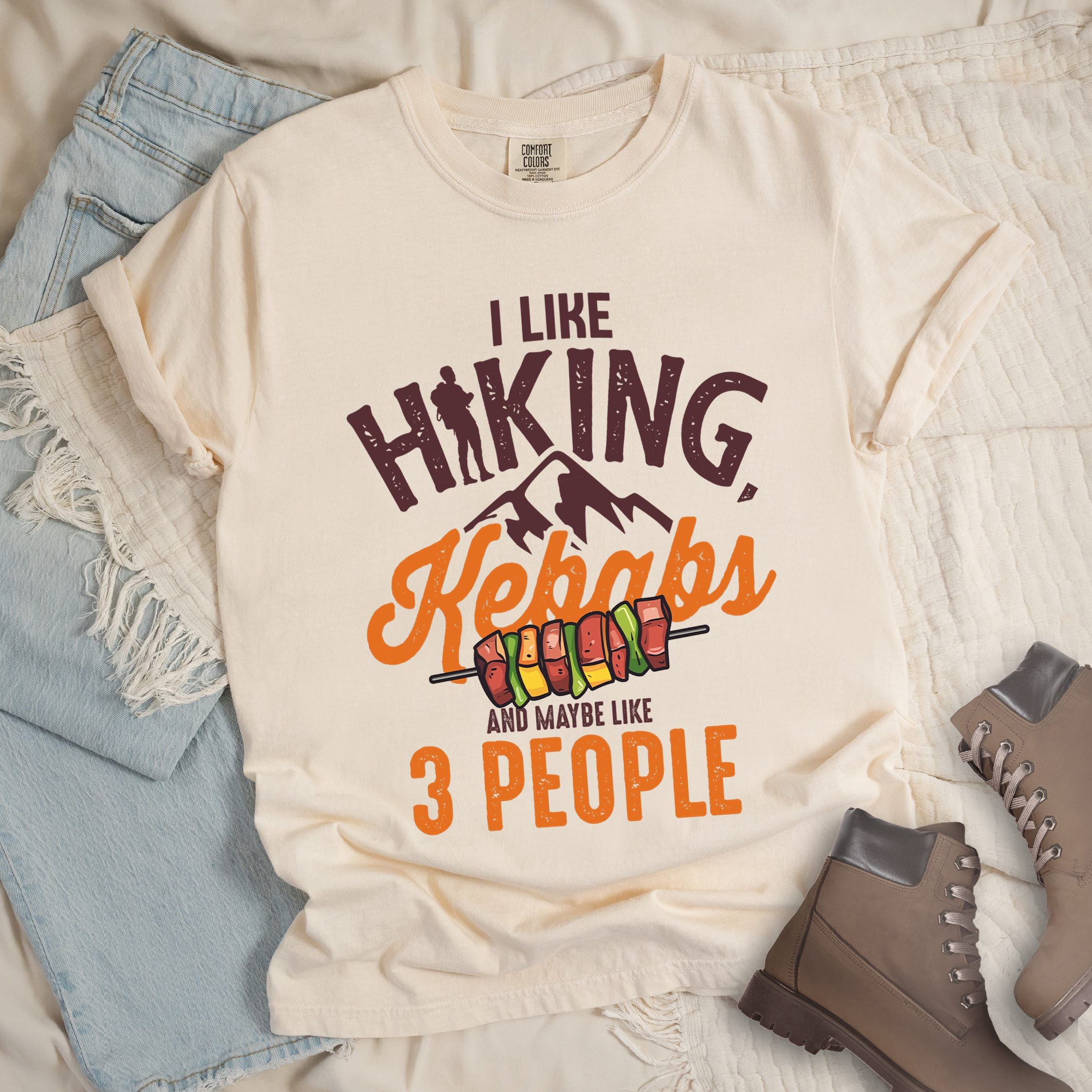 Ivory shirt with “I Like Hiking, Kebabs and Maybe Like 3 People” in white and orange text, featuring a hiker silhouette, mountain outline, and skewers of colorful kebabs.