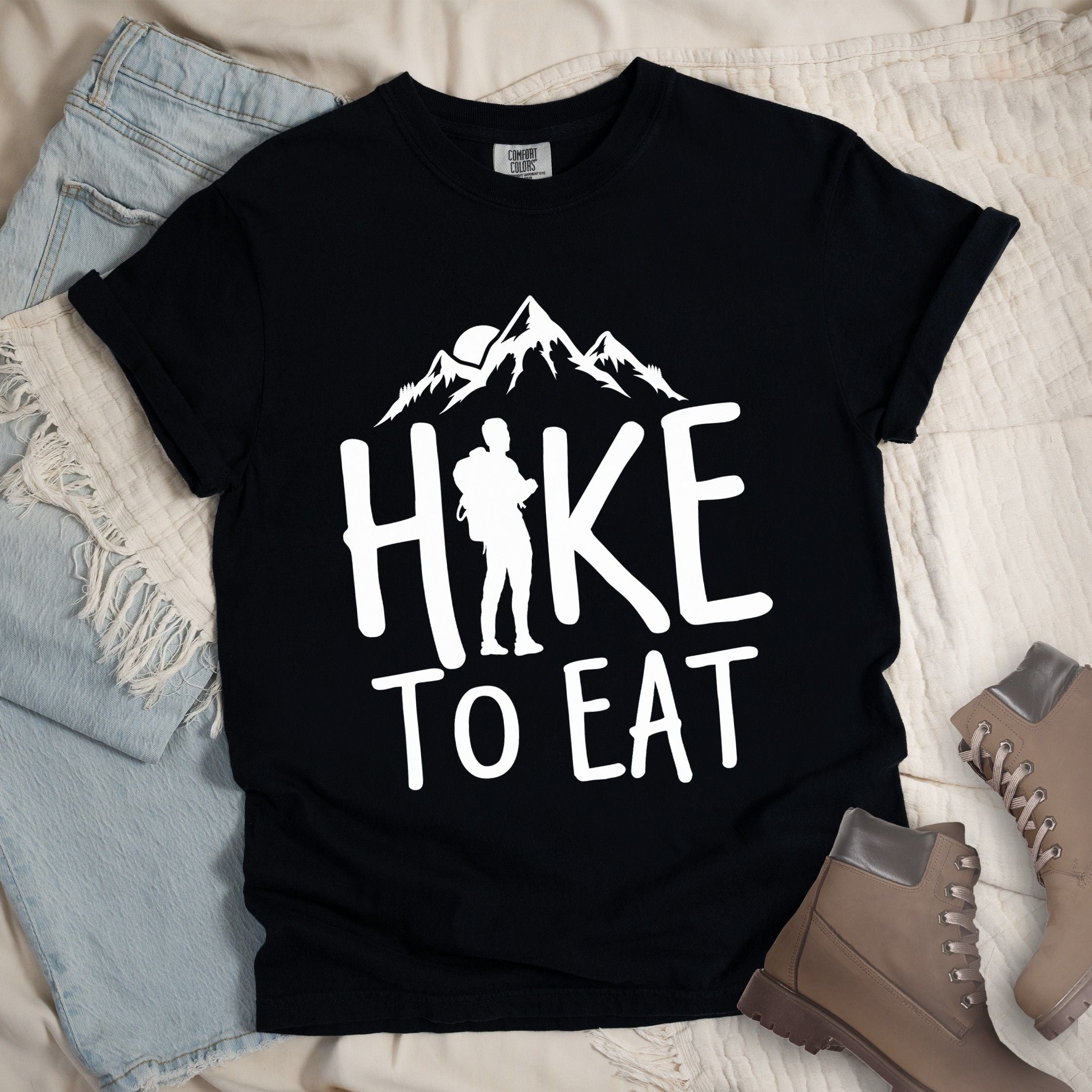 Black shirt with a Hiking design featuring mountain silhouette and shows 'Hike To Eat' phrase in bold text