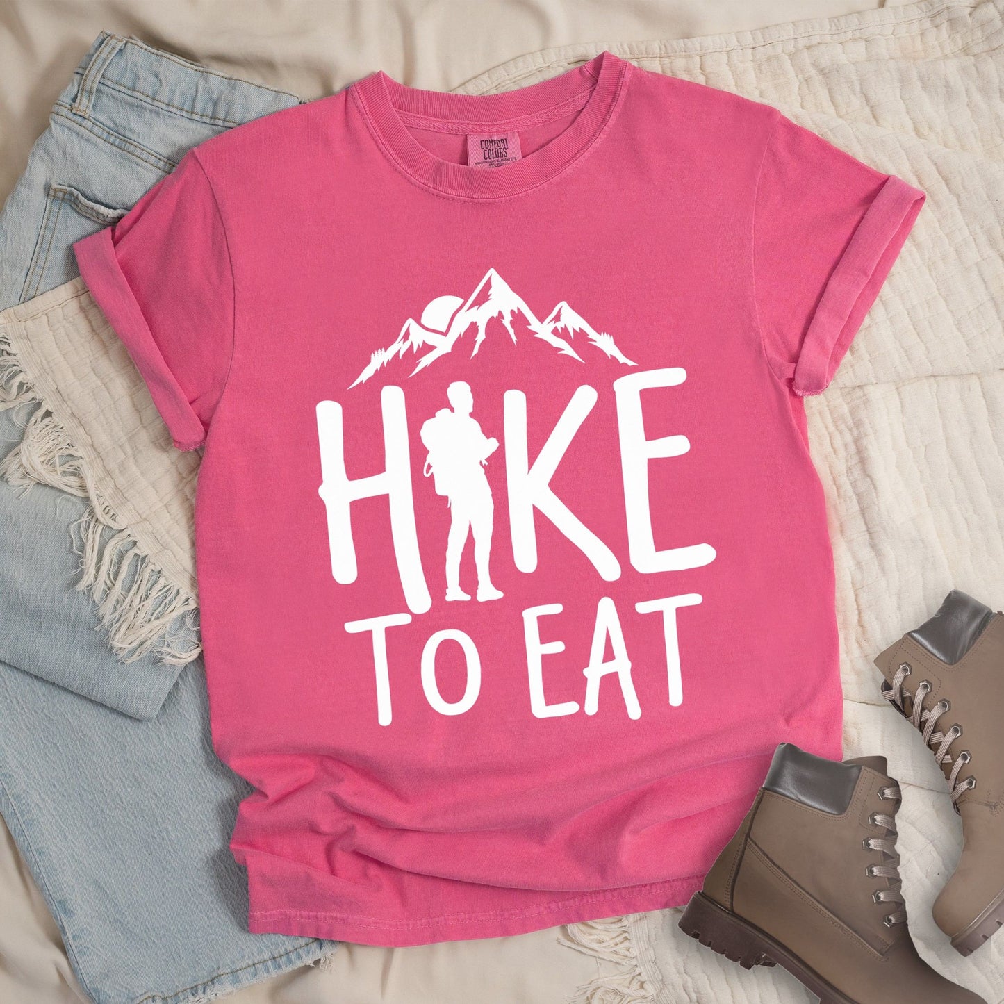 Pink shirt with a Hiking design featuring mountain silhouette and shows 'Hike To Eat' phrase in bold text