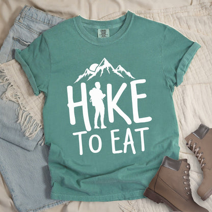 Green shirt with a Hiking design featuring mountain silhouette and shows 'Hike To Eat' phrase in bold text