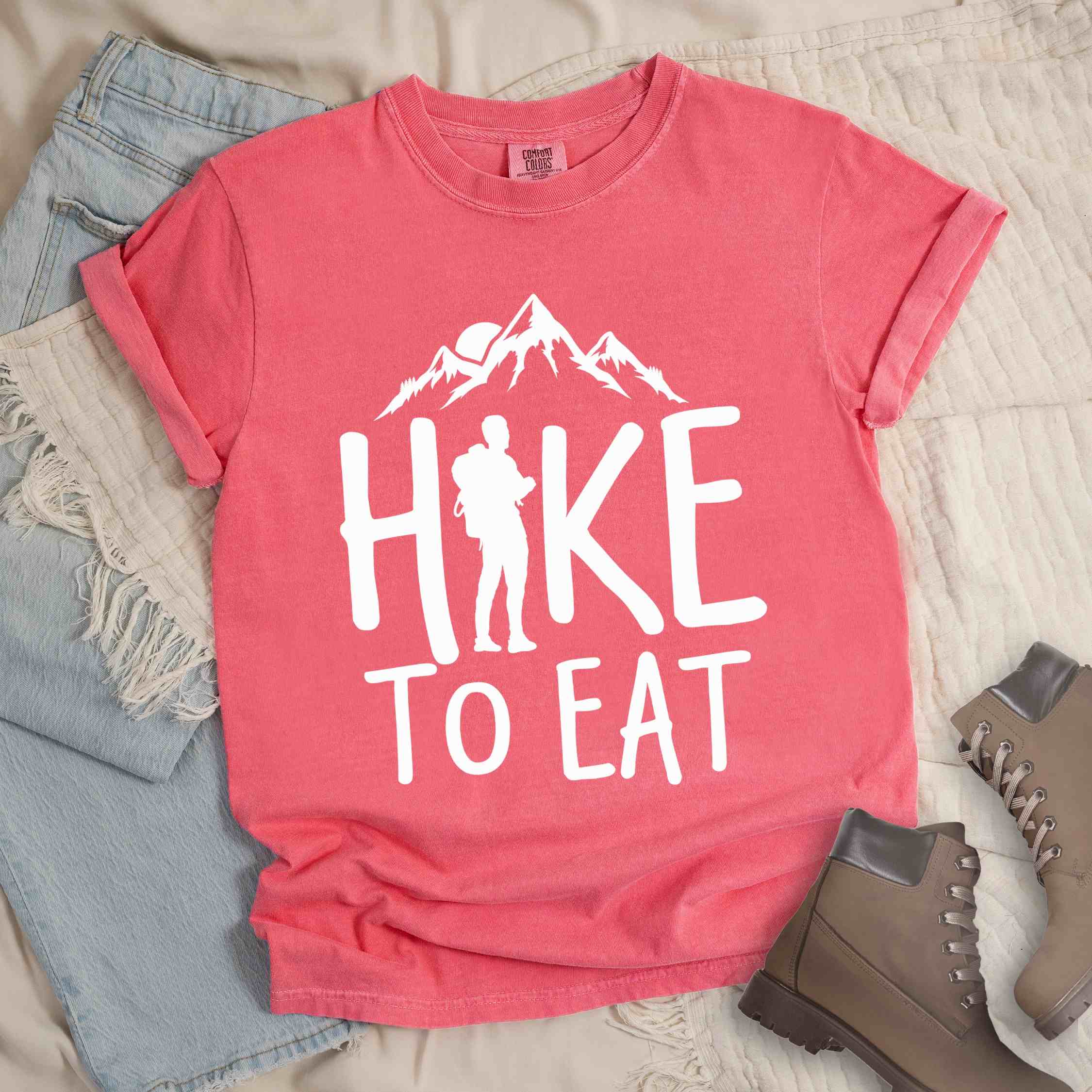 Watermelon "Hike to Eat" colored statement tee with bold typography, mountains, birds, sunrise, perfect for food motivated individuals.