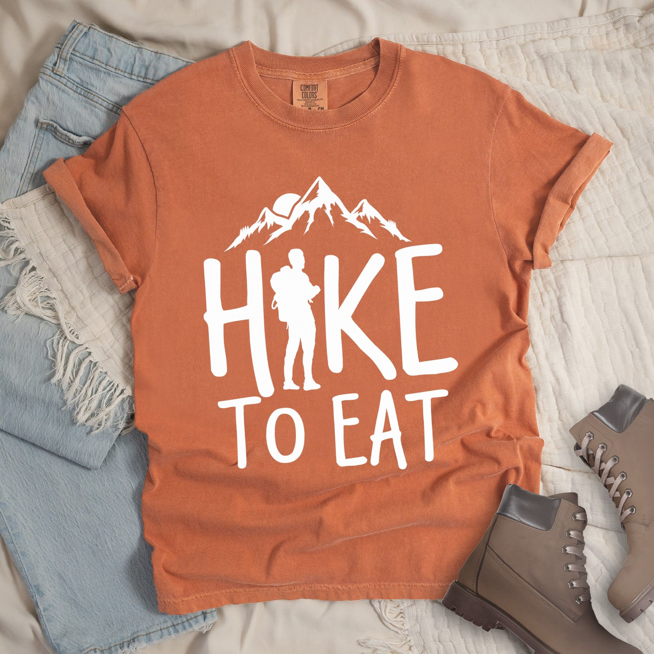 Orange shirt with a Hiking design featuring mountain silhouette and shows 'Hike To Eat' phrase in bold text