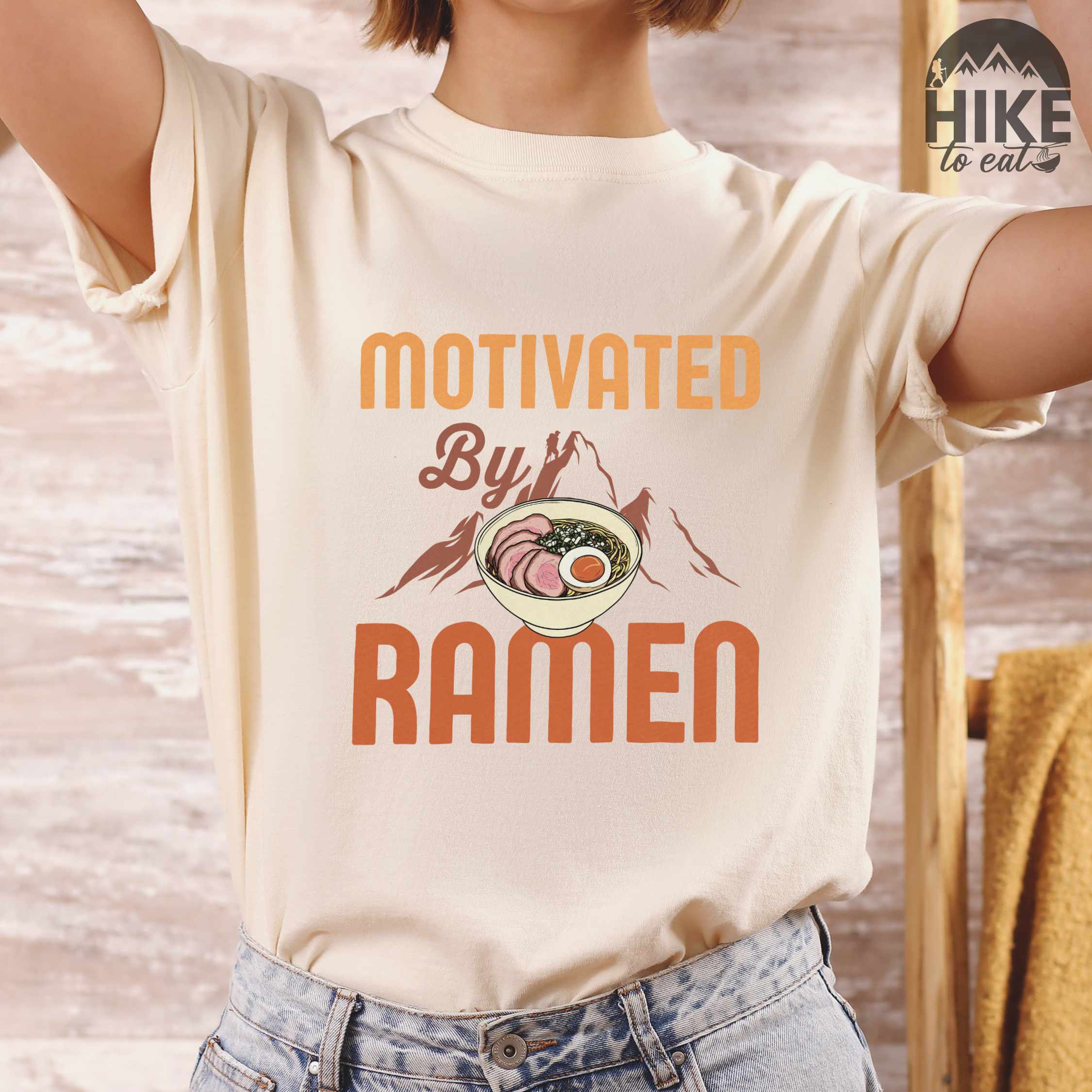 Woman wearing ivory “Motivated by Ramen” colored vintage tee with bold text, mountain, Illustration of hot ramen. Perfect tee for foodie craving for a bowl of ramen,