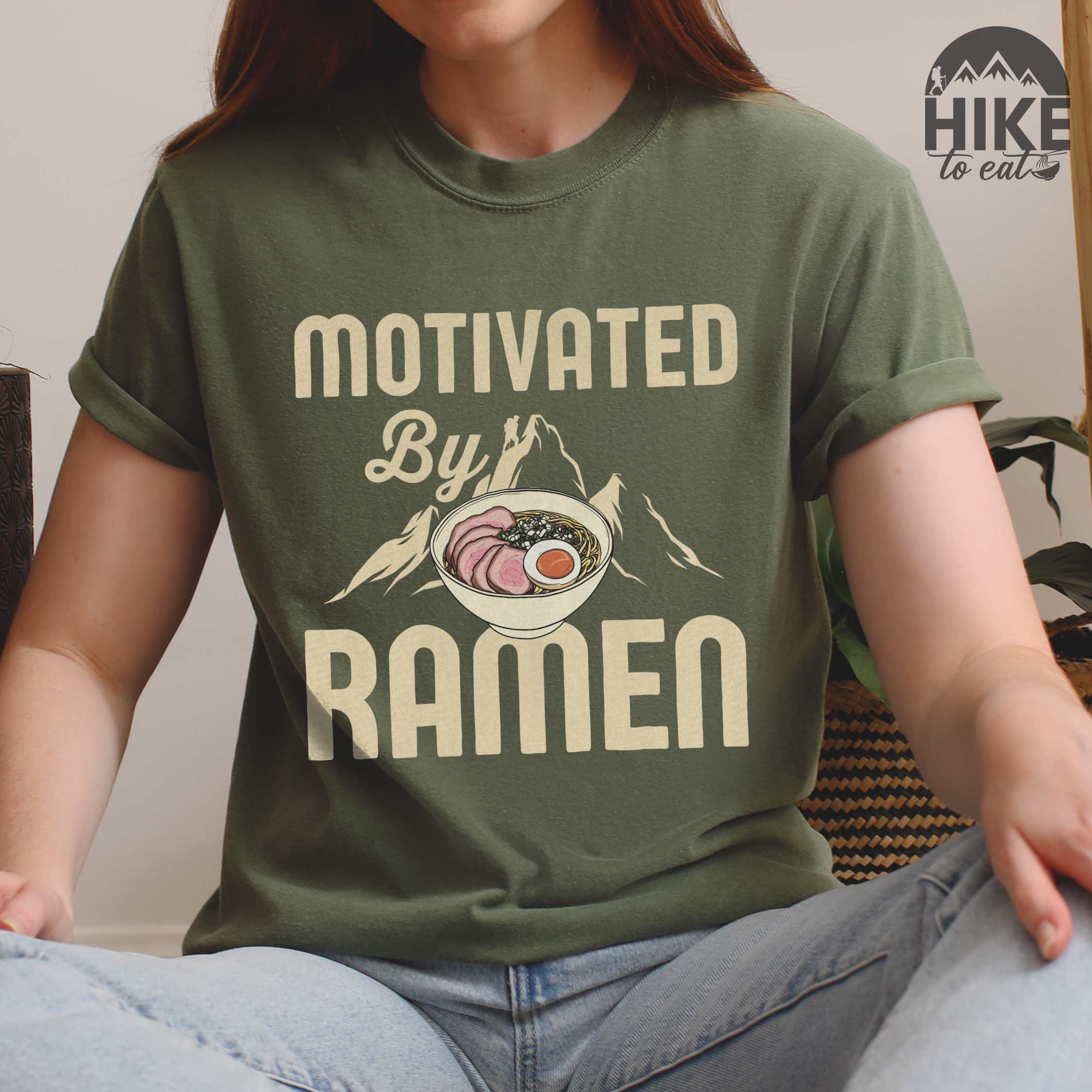 Woman wearing moss “Motivated by Ramen” colored vintage tee with bold text, mountain, Illustration of hot ramen. Perfect tee for foodie craving for a bowl of ramen,