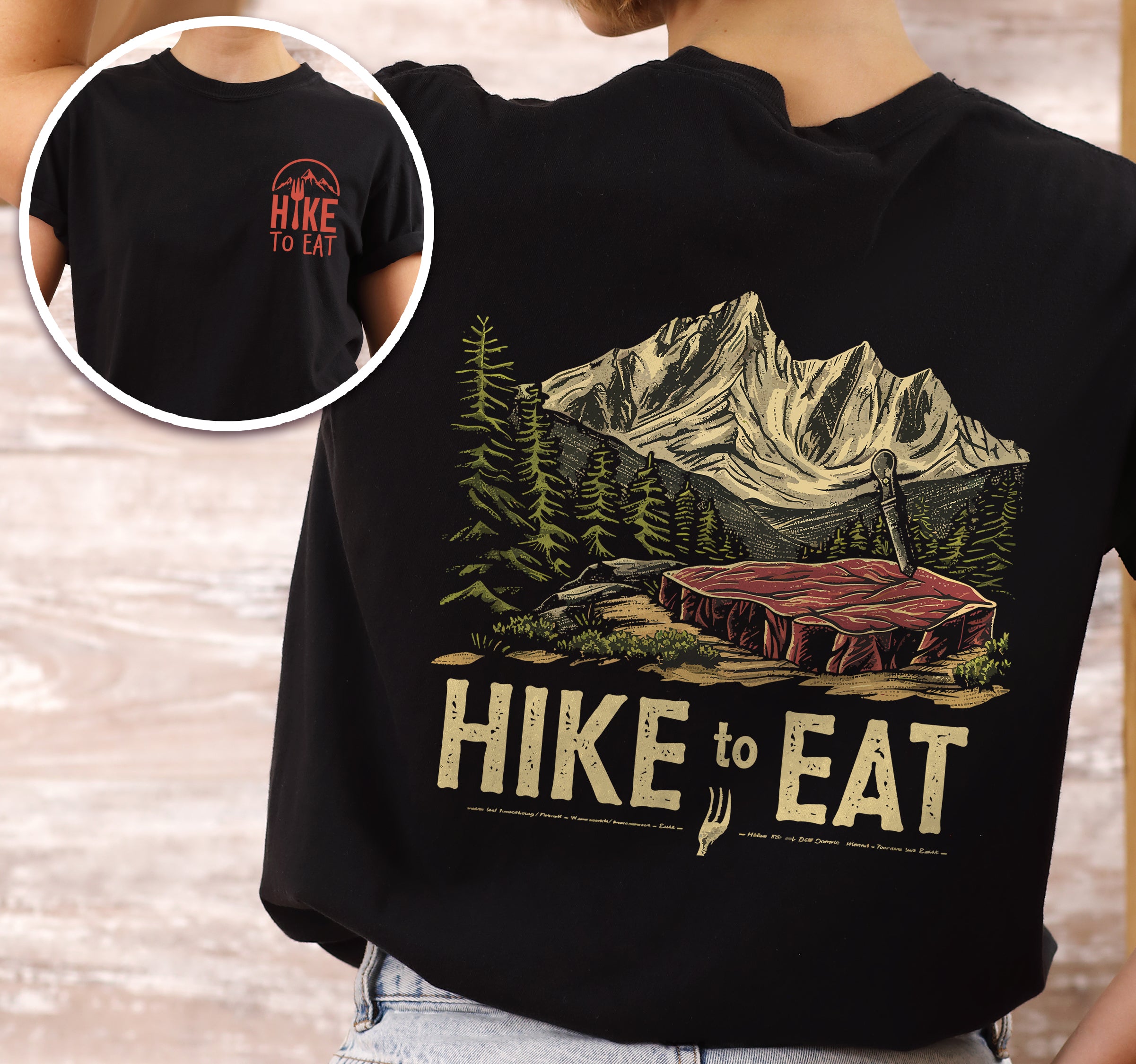 Black Hike to Eat t-shirt front and back view showing small chest logo and large back design featuring raw steak in mountain wilderness landscape with pine trees worn by a female person. 