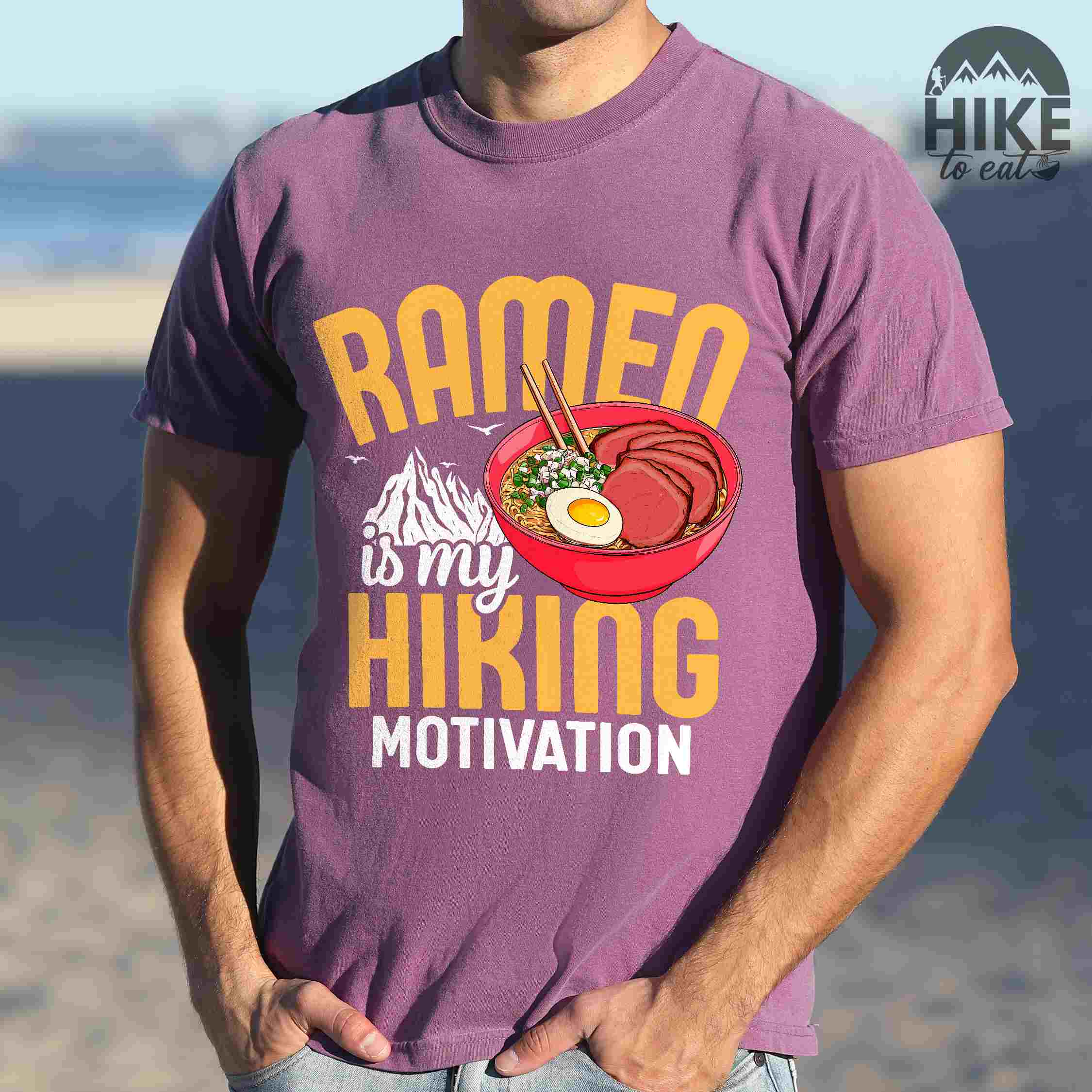 Man wearing berry “Ramen is my Hiking motivation” colored vintage tee with bold text, mountain, Illustration of hot ramen. Perfect tee for foodie craving for a bowl of ramen,