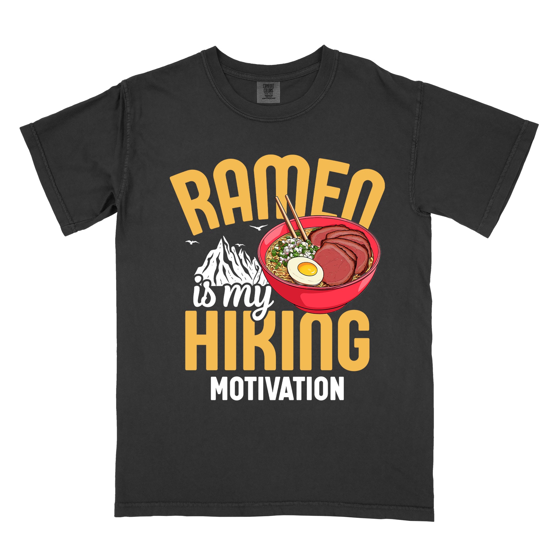 Black t-shirt with "RAMEN is my HIKING MOTIVATION" text design. "RAMEN" and "HIKING" appear in large yellow letters, with "is my" in white script and "MOTIVATION" in white capitals. The design features a colorful illustration of a red ramen bowl with sliced meat, egg, green onions, and chopsticks. A white mountain silhouette appears between "RAMEN" and "HIKING", with small bird silhouettes nearby.