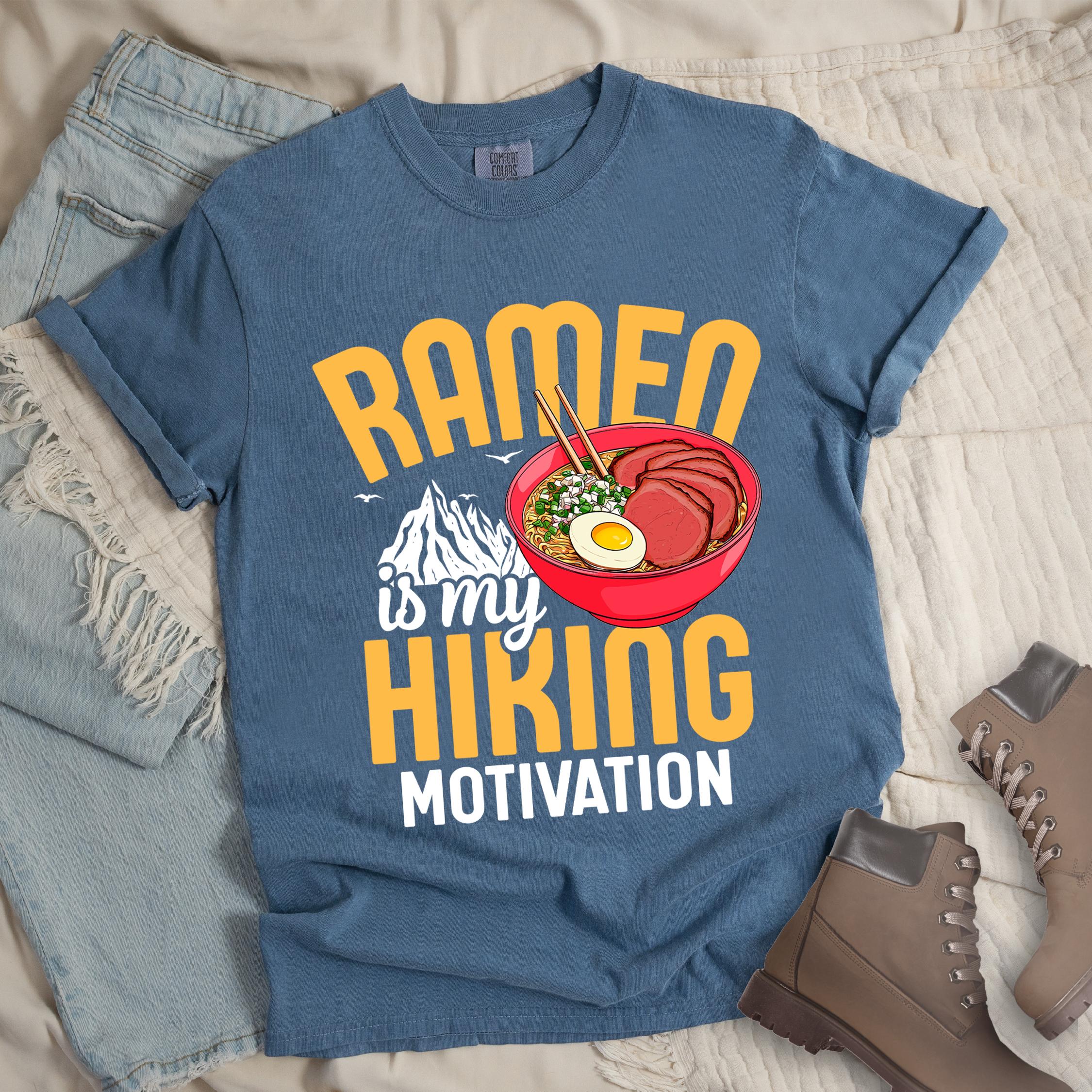 Dark blue shirt with “Ramen is my Hiking Motivation” text, featuring a mountain graphic and a ramen bowl with noodles, egg, meat, and chopsticks.