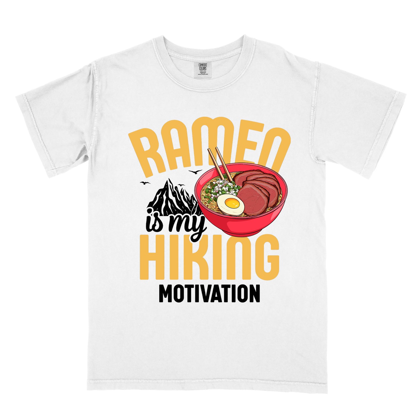 White t-shirt with "RAMEN is my HIKING MOTIVATION" text design. "RAMEN" and "HIKING" appear in large yellow letters, with "is my" in black script and "MOTIVATION" in black capitals. The design features a colorful illustration of a red ramen bowl with sliced meat, egg, green onions, and chopsticks. A black mountain silhouette appears between "RAMEN" and "HIKING", with small bird silhouettes nearby.
