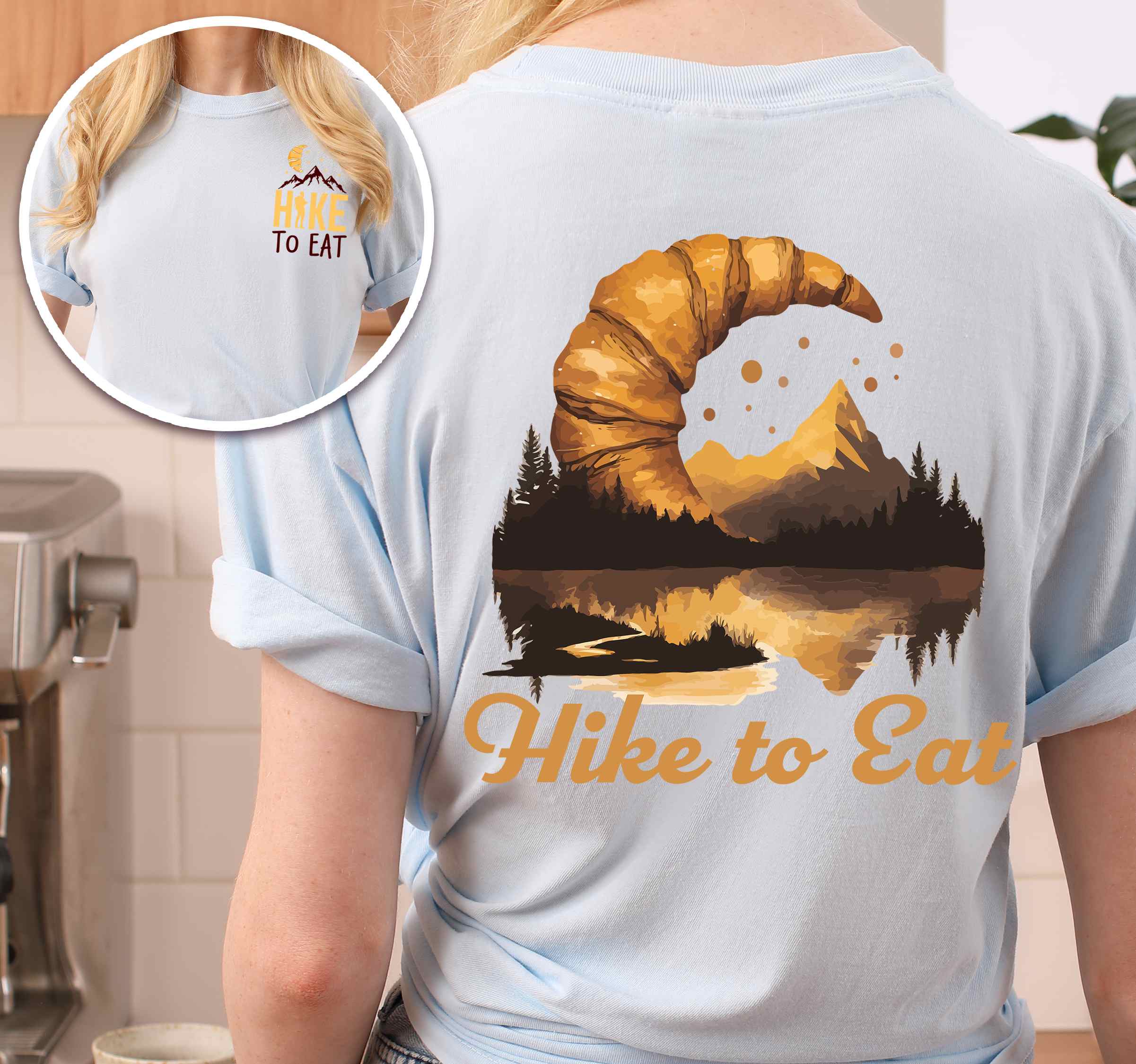 Woman wearing chambray "Hike to Eat" text in cream lettering, mountains, birds, illustrated baked croissant moon, and backpacker for pastry enthusiasts.