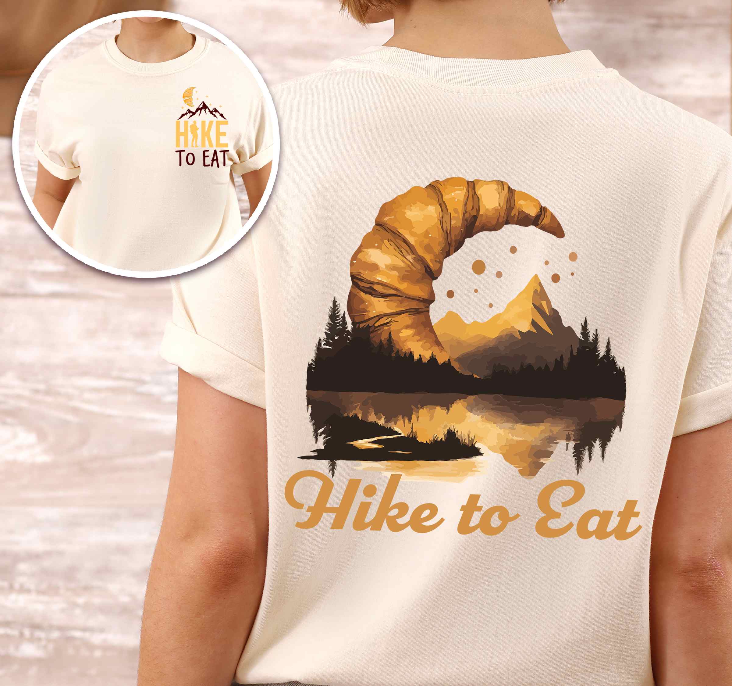 Woman wearing ivory "Hike to Eat" text in cream lettering, mountains, birds, illustrated baked croissant moon, and backpacker for pastry enthusiasts.