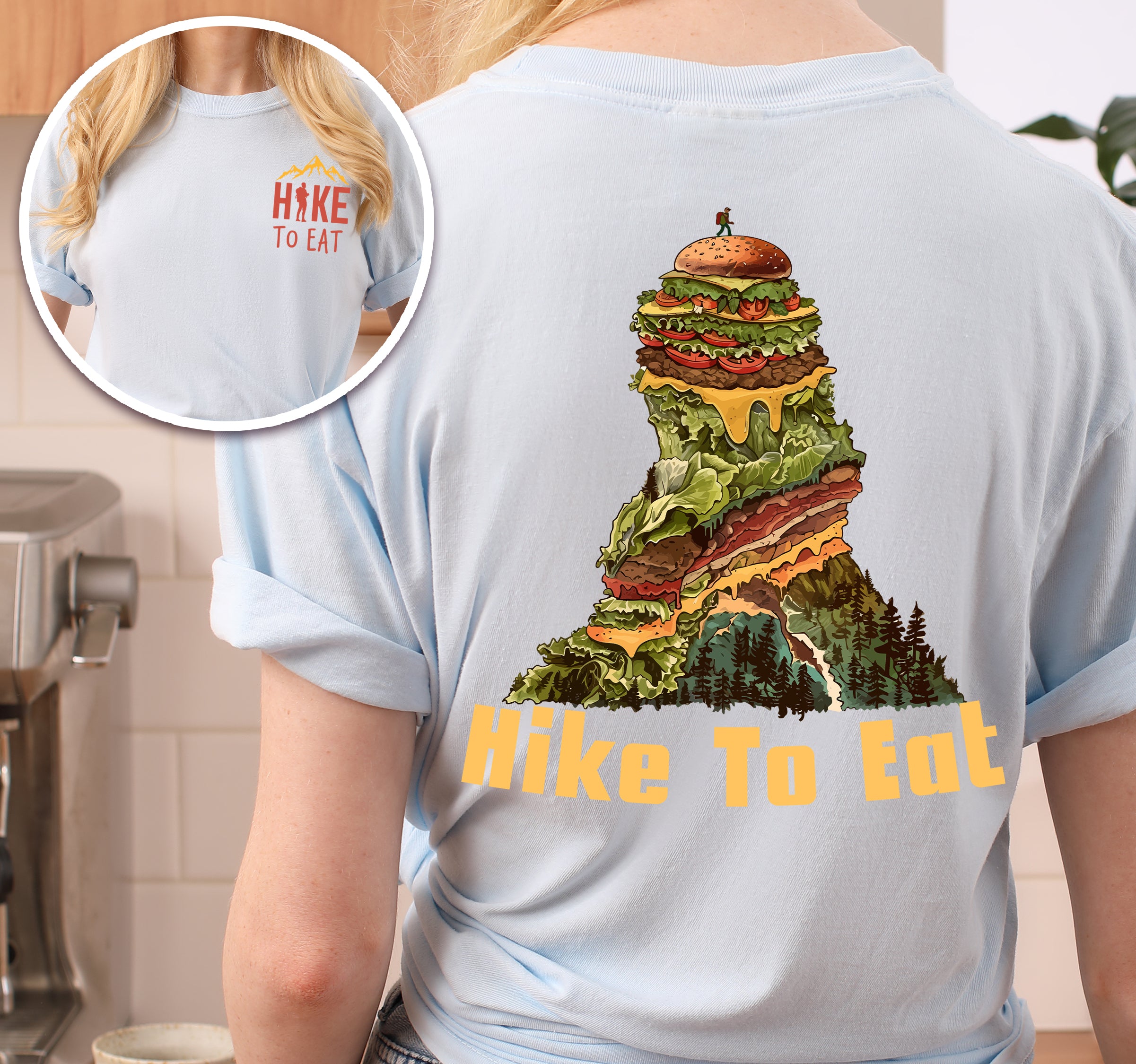 Chambray (Light Blue) Hike to Eat t-shirt front and back view showing small orange chest logo and large back design featuring mountain-shaped burger stack with multiple layers, lettuce, cheese, and pine forest at the base.