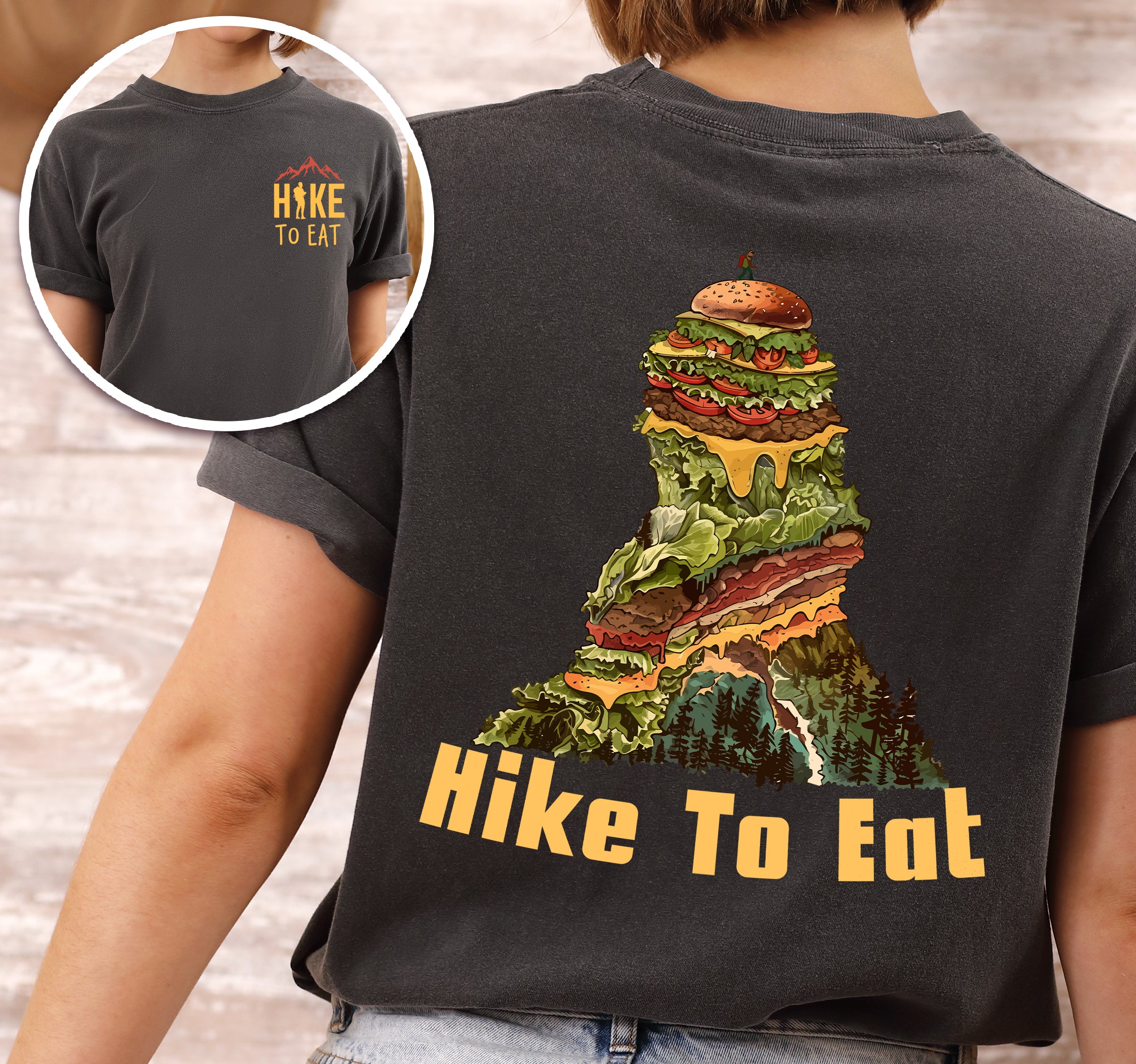 Pepper (Dark Gray) Hike to Eat t-shirt front and back view showing small orange chest logo and large back design featuring mountain-shaped burger stack with multiple layers, lettuce, cheese, and pine forest at the base.