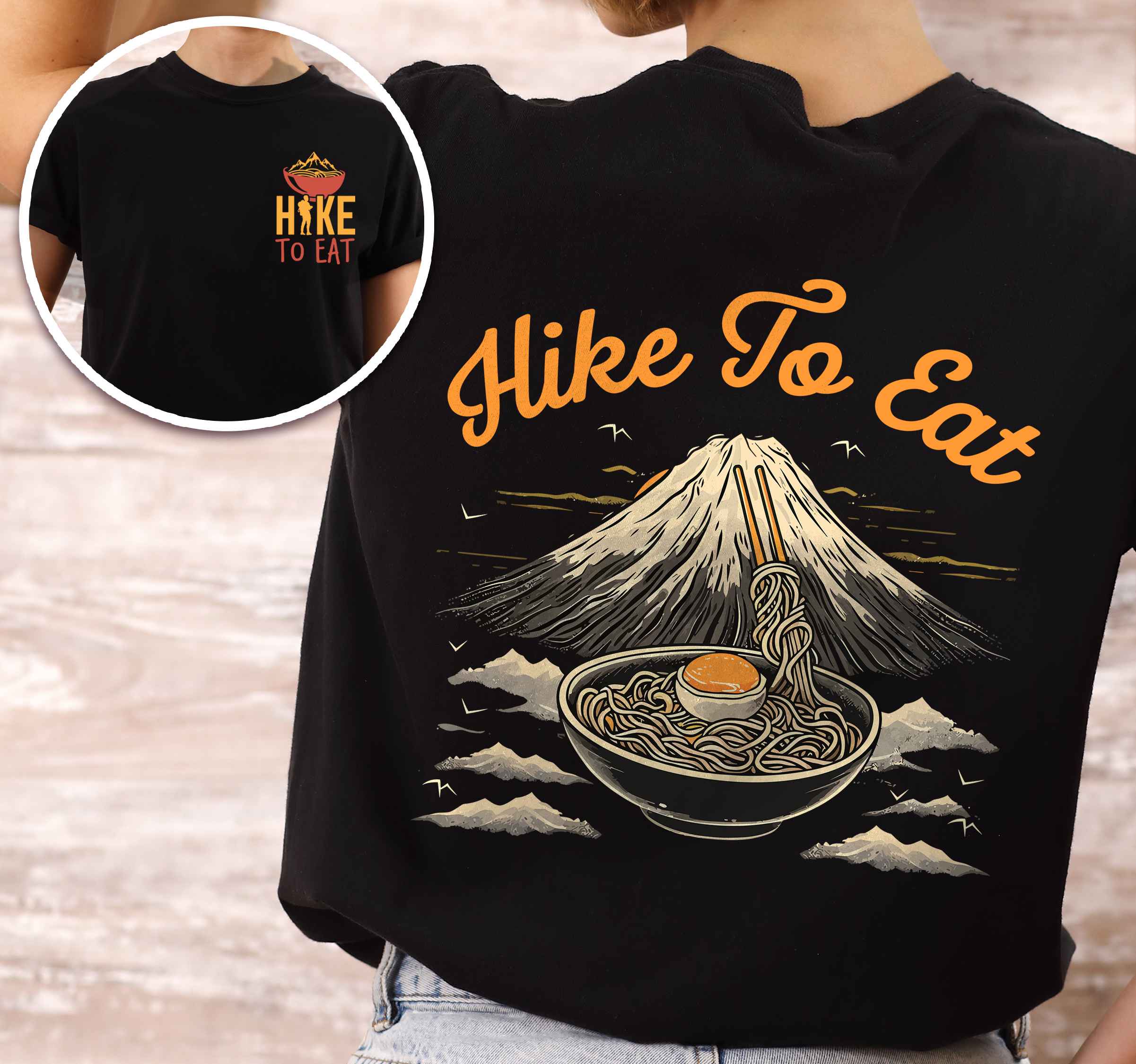 woman wearing black "Hike to Eat" text in bold lettering front and back design, mountains, birds, illustrated bowl of ramen noodles, and backpacker for ramen lovers.