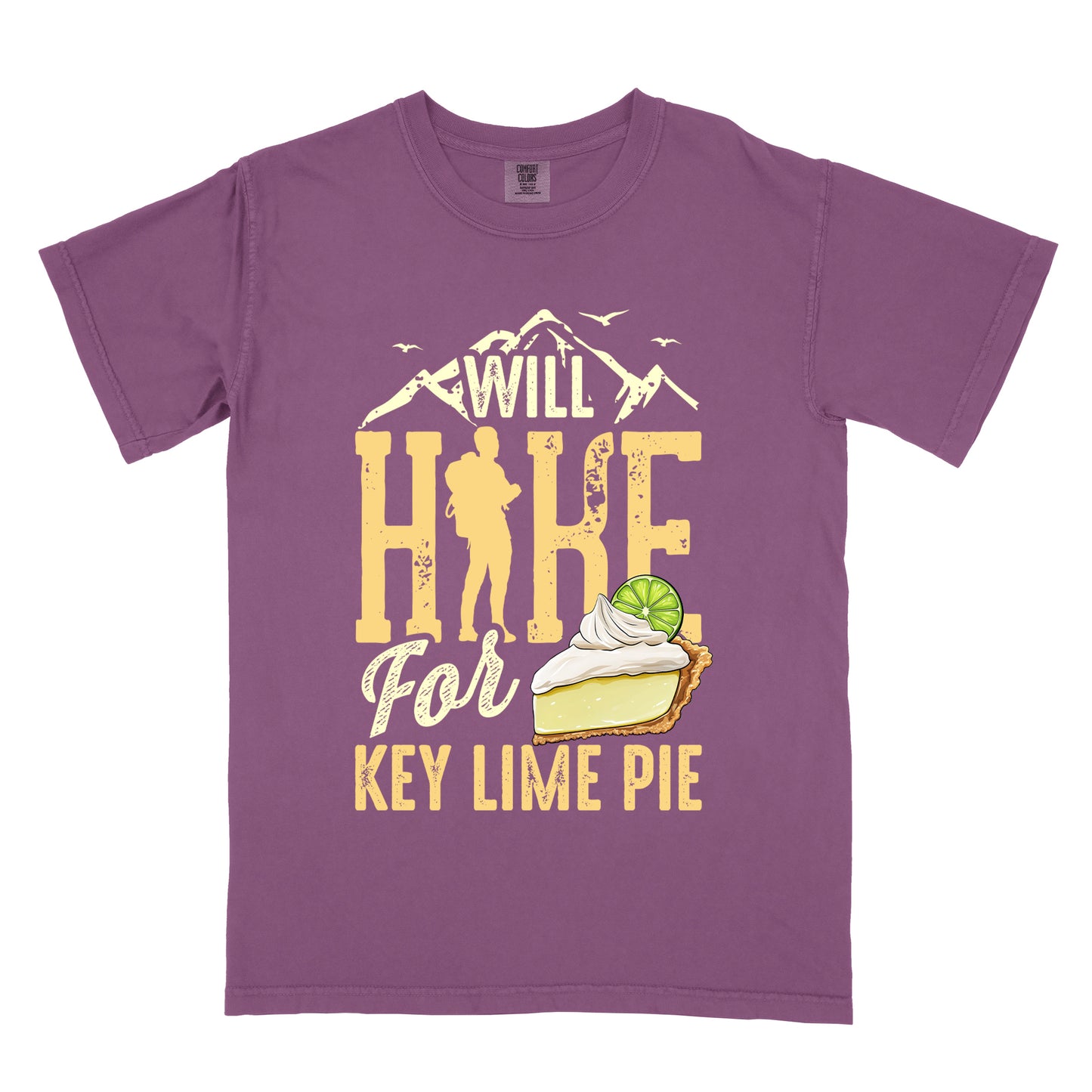 Berry (Dark Violet) t-shirt with text "WILL HIKE For KEY LIME PIE" in yellow tones. "WILL" appears in cream letters within mountain silhouettes with flying birds. "HIKE" is in large distressed yellow letters with a hiker silhouette replacing the "I". "For" appears in cream script, and "KEY LIME PIE" in yellow block letters. An illustration of a key lime pie slice with whipped cream and lime garnish appears next to "For" and above "KEY LIME PIE".