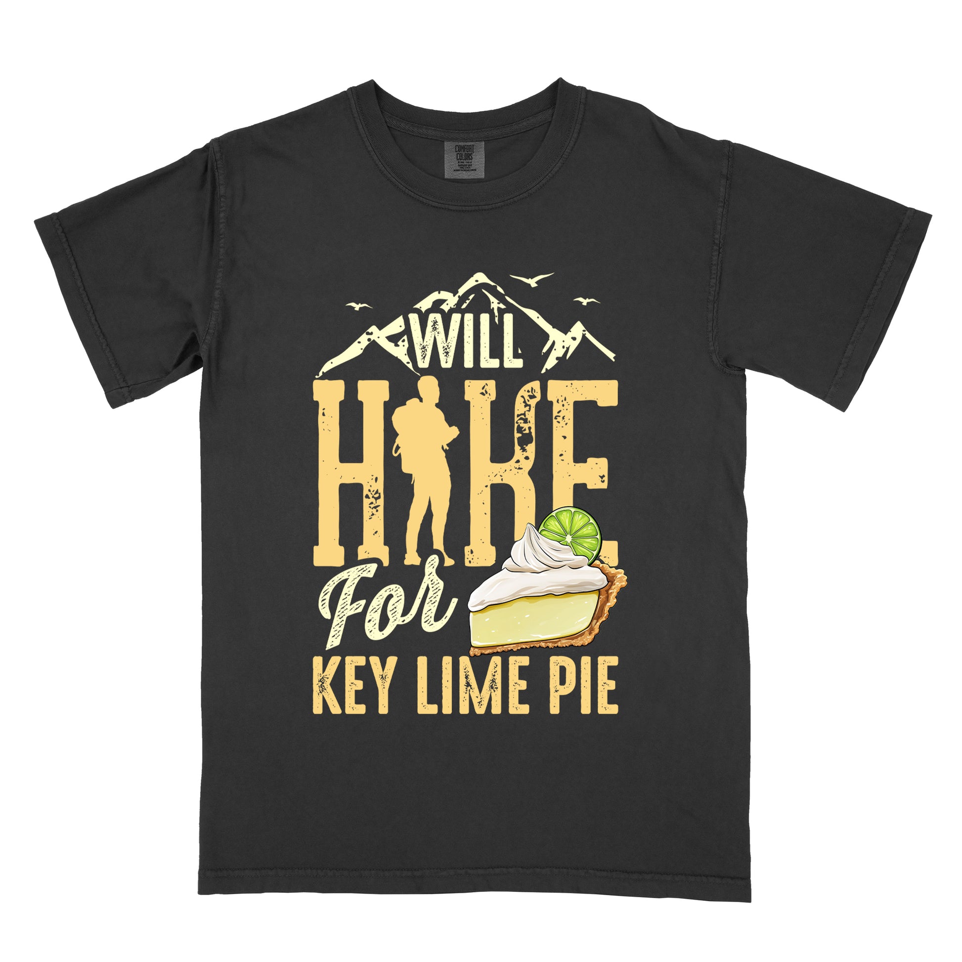 Black t-shirt with text "WILL HIKE For KEY LIME PIE" in yellow tones. "WILL" appears in cream letters within mountain silhouettes with flying birds. "HIKE" is in large distressed yellow letters with a hiker silhouette replacing the "I". "For" appears in cream script, and "KEY LIME PIE" in yellow block letters. An illustration of a key lime pie slice with whipped cream and lime garnish appears next to "For" and above "KEY LIME PIE".