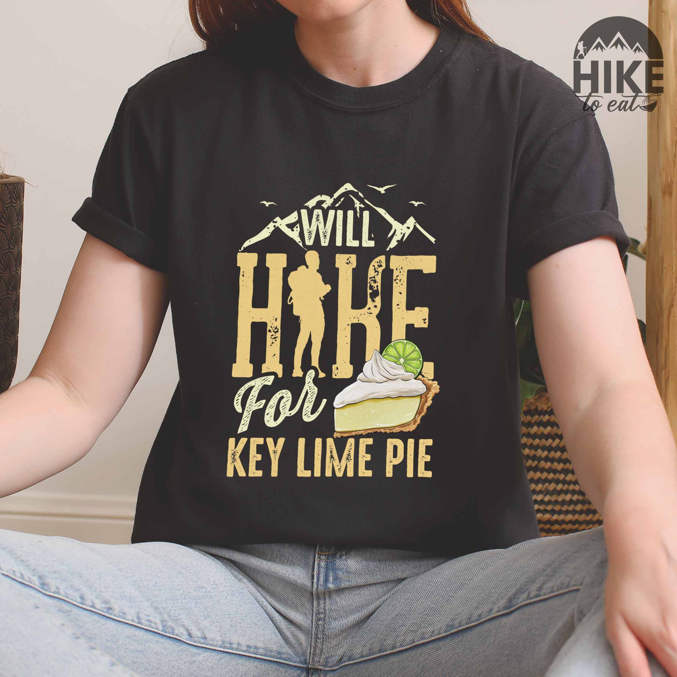 Woman wearing black "Will Hike for Key Lime Pie" colored vintage tee with bold typography, illustrated slice of key lime pie, mountains, birds, and backpacker with the sweet tooth.
