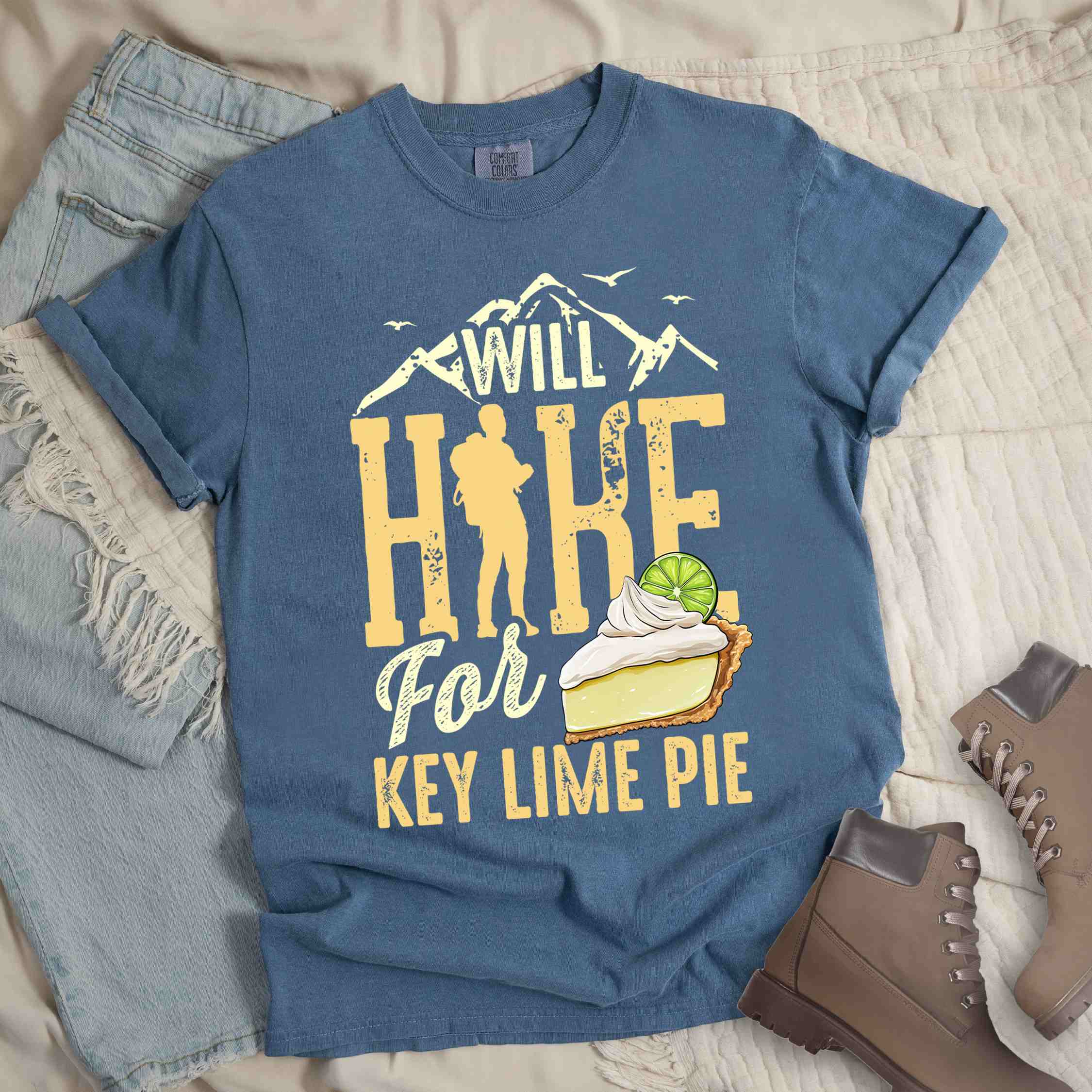 Blue jean "Will Hike for Key Lime Pie" colored vintage tee with bold typography, illustrated slice of key lime pie, mountains, birds, and backpacker with the sweet tooth.