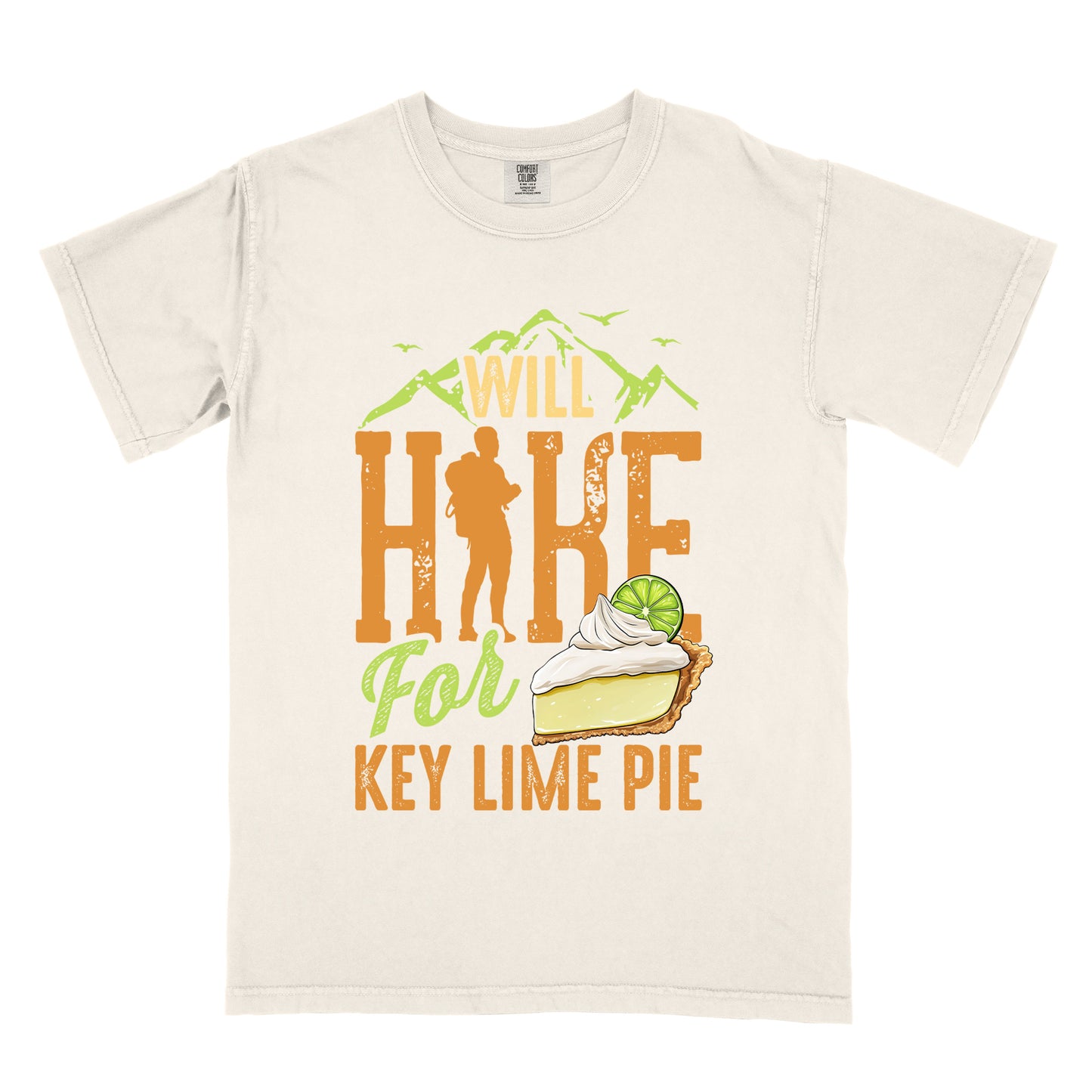 Ivory (Cream White) t-shirt with text "WILL HIKE For KEY LIME PIE" in orange and green tones. "WILL" appears in cream letters within mountain silhouettes with flying birds. "HIKE" is in large distressed orange letters with a hiker silhouette replacing the "I". "For" appears in light green script, and "KEY LIME PIE" in orange block letters. An illustration of a key lime pie slice with whipped cream and lime garnish appears next to "For" and above "KEY LIME PIE".