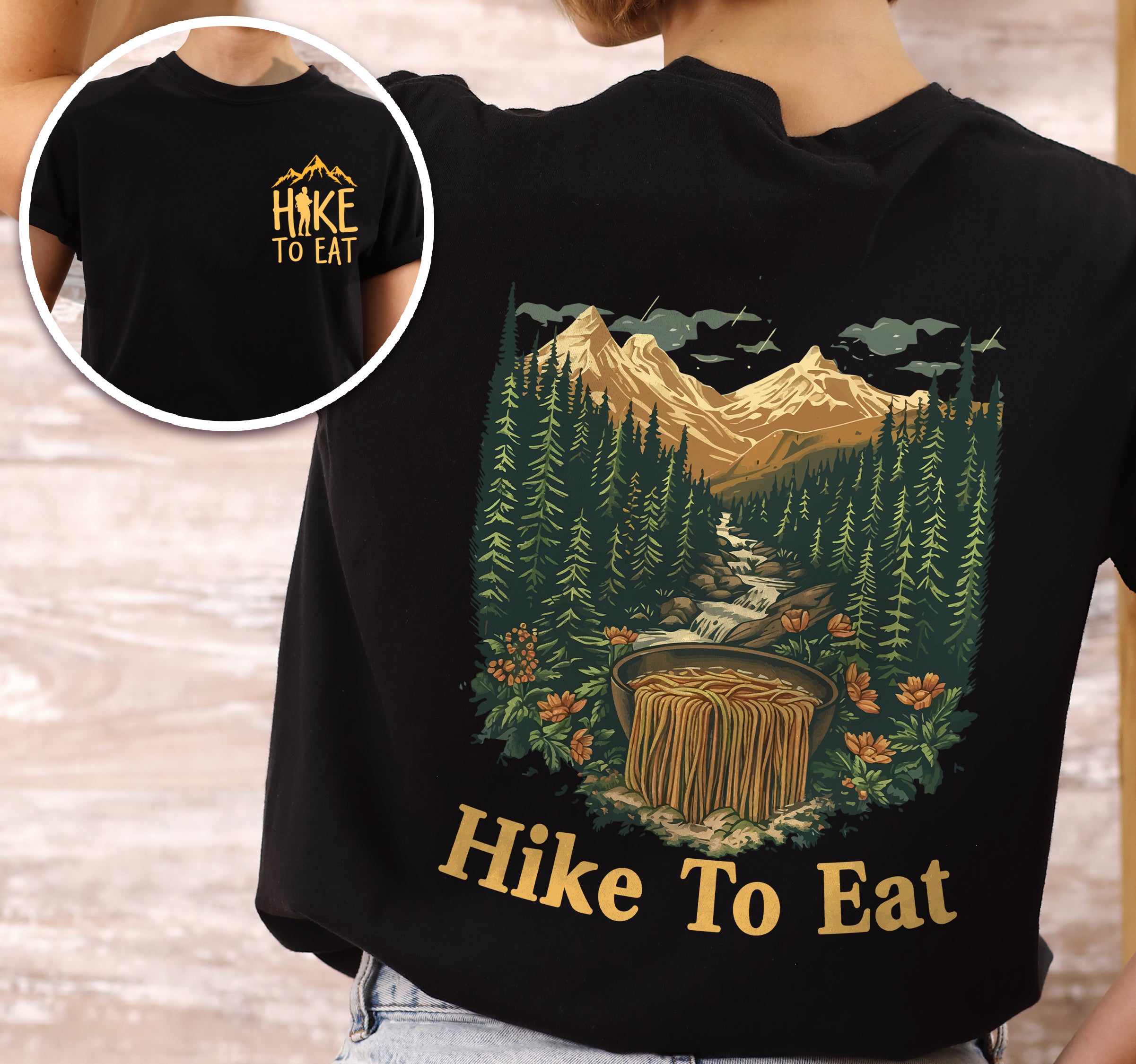 Black Hike to Eat t-shirt front and back view showing small colorful chest detail and large back design featuring mountain landscape with crystal-clear stream cascading through evergreen forests and wildflowers, transforming into flowing ramen noodles in a rustic wooden bowl.