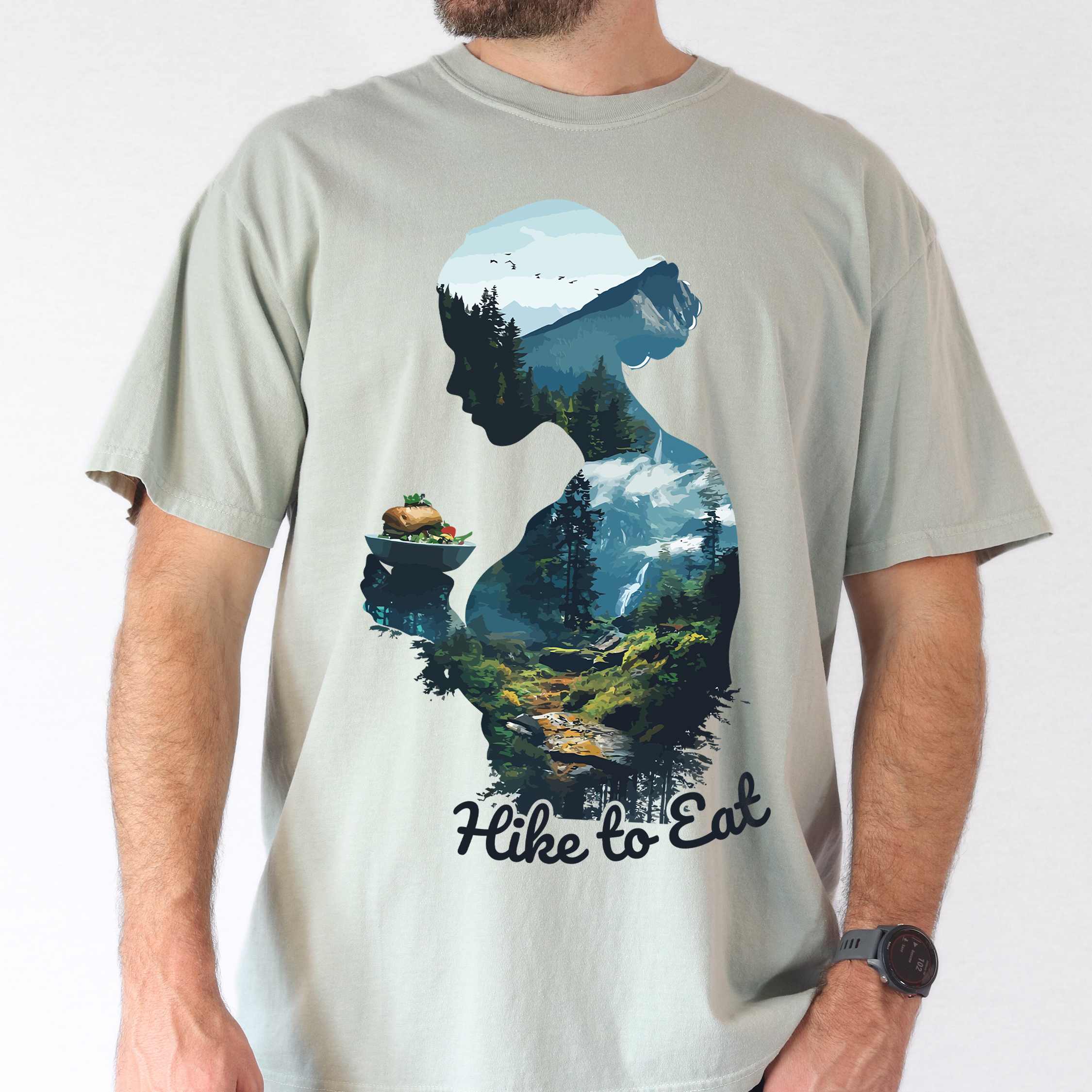 Man wearing bay "Hike to Eat" colored vintage statement tee with text in cream lettering, mountains, birds, silhouette, illustrated sandwich, and backpacker for sandwich lovers.