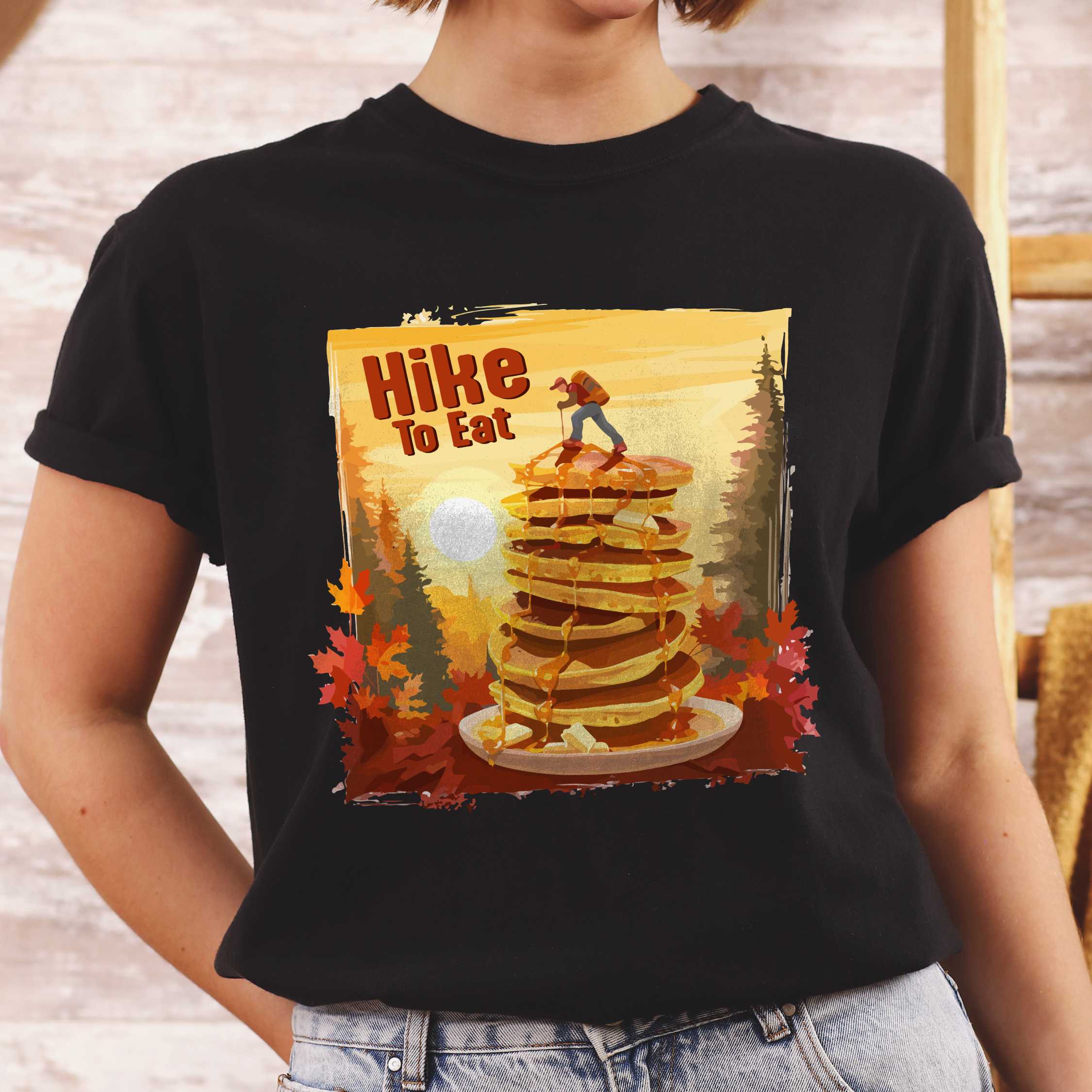 Woman wearing black "Hike to Eat" colored vintage statement tee with text in bold lettering, mountains, birds, silhouette, illustrated stack of pancake, and perfect for breakfast lovers.