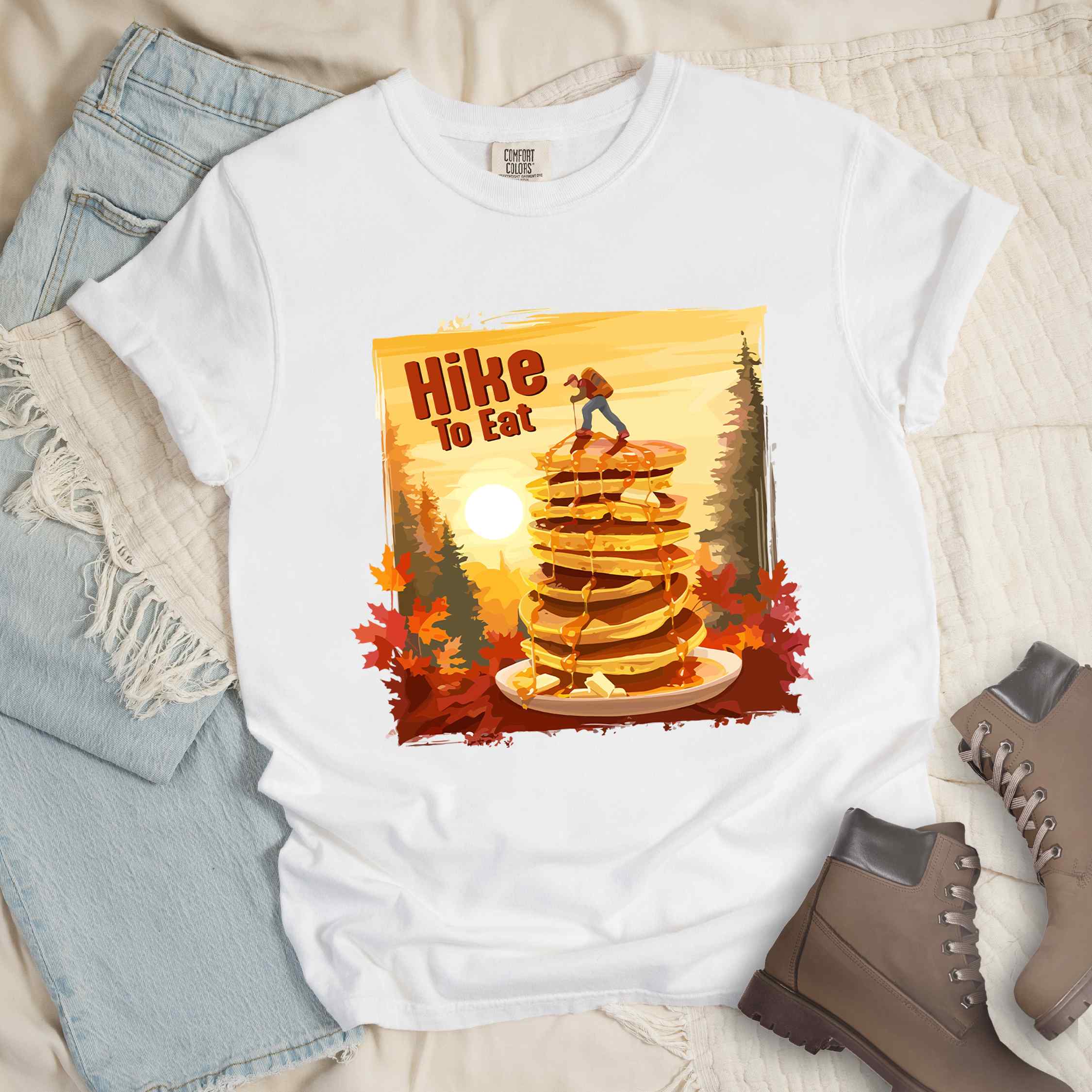 White "Hike to Eat" colored vintage statement tee with text in Bold lettering, mountains, birds, silhouette, illustrated stack of pancake, and perfect for breakfast lovers.