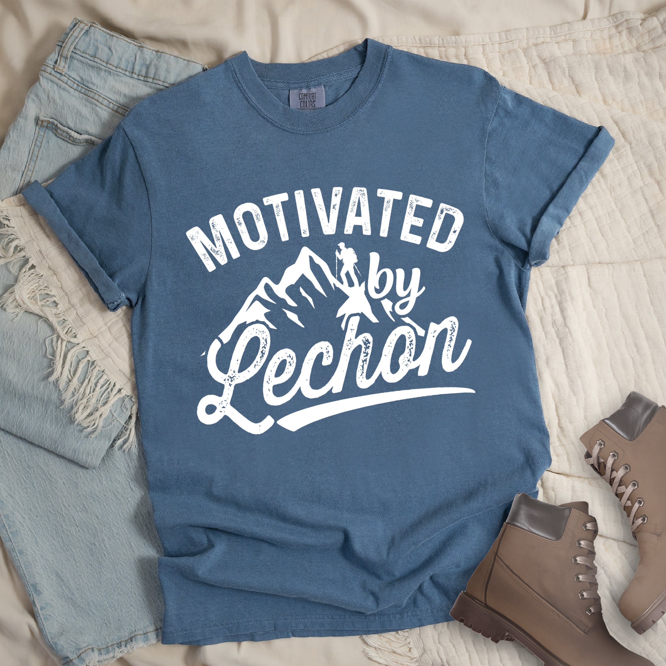 Blue Jean (Denim Blue) graphic t-shirt with 'Motivated by Lechon' text in white lettering featuring mountain silhouettes and hiker illustration