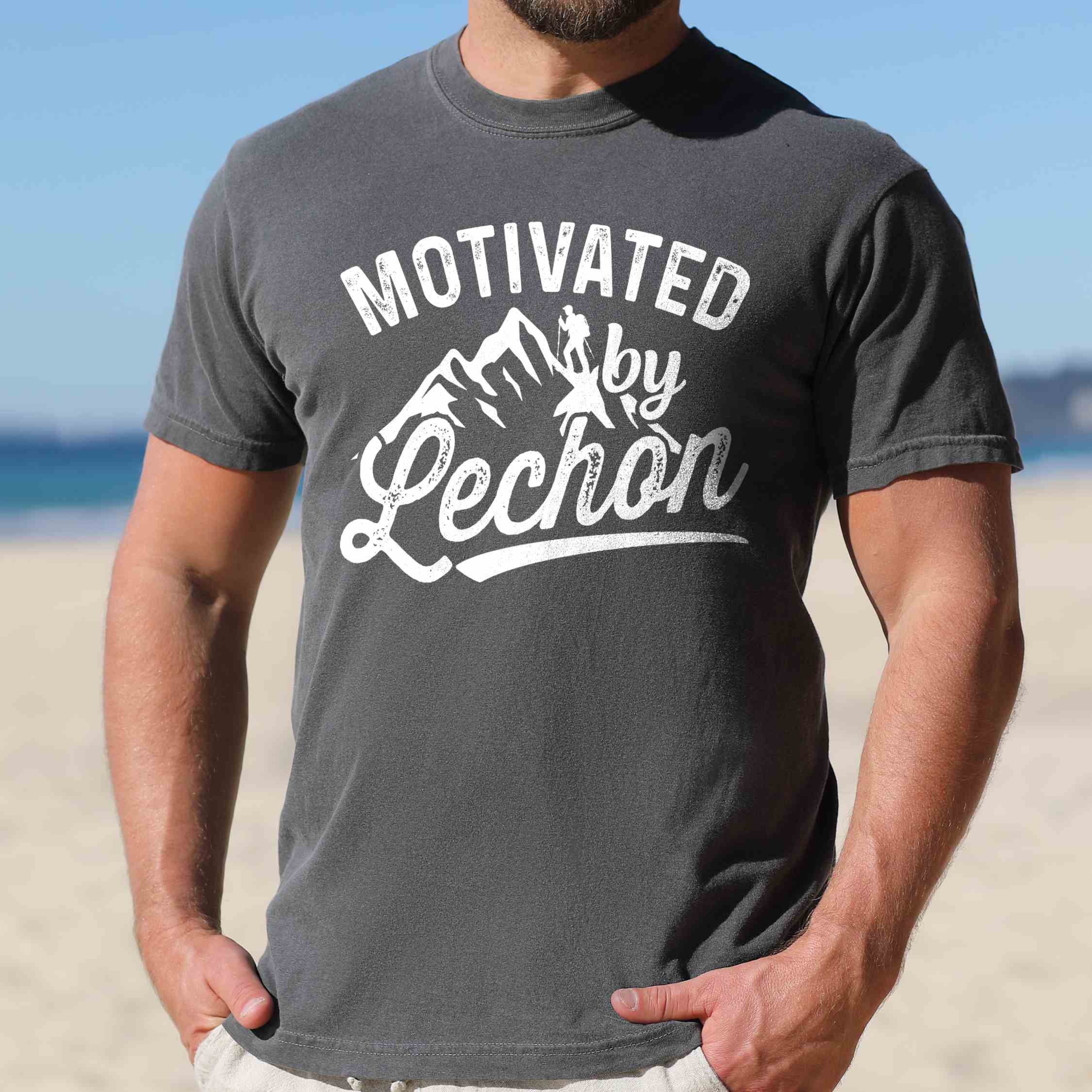 Man wearing pepper colored graphic t-shirt with 'Motivated by Lechon' text in white lettering featuring mountain silhouettes and hiker illustration