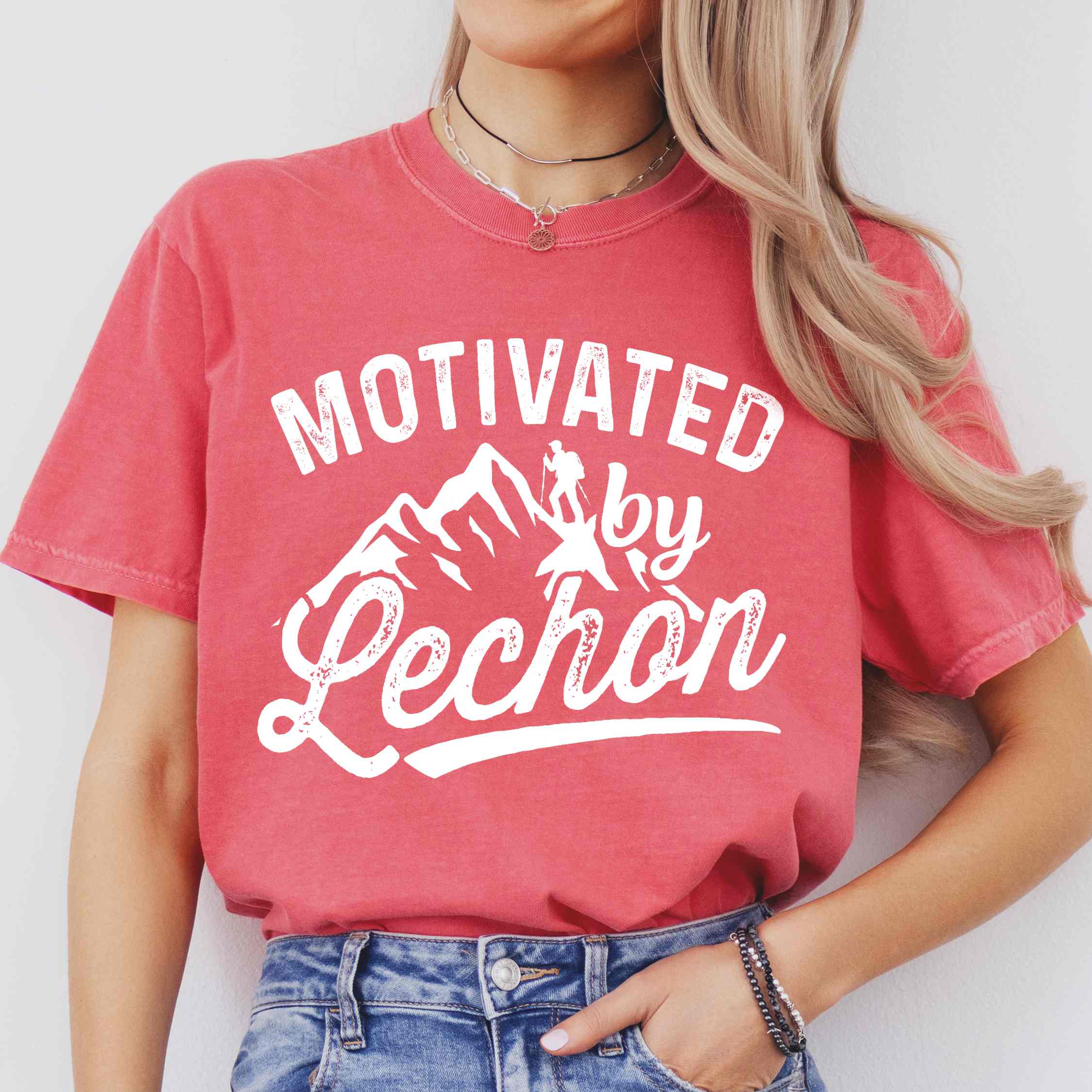 Woman wearing watermelon colored graphic t-shirt with 'Motivated by Lechon' text in white lettering featuring mountain silhouettes and hiker illustration