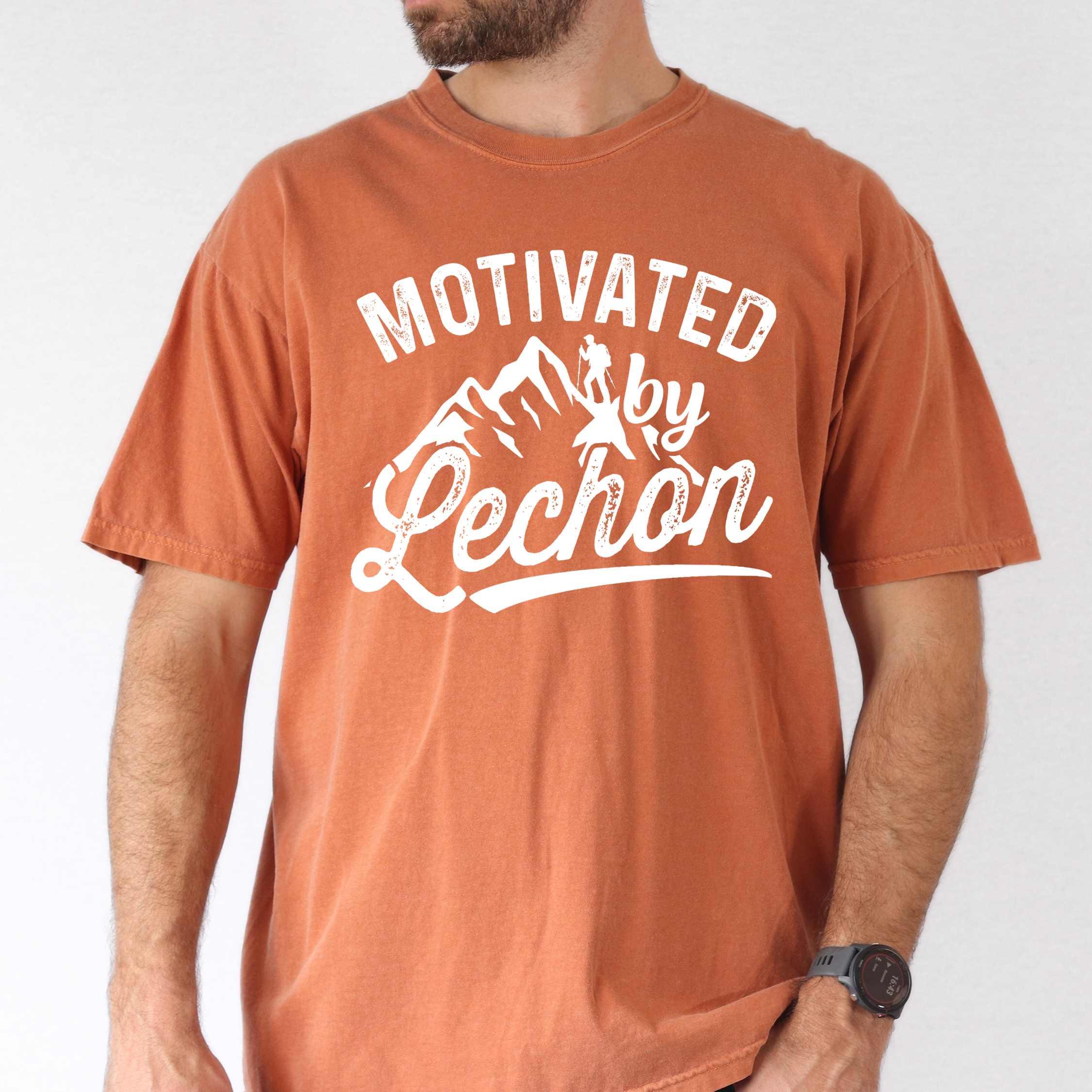 Man wearing yam colored graphic t-shirt with 'Motivated by Lechon' text in white lettering featuring mountain silhouettes and hiker illustration