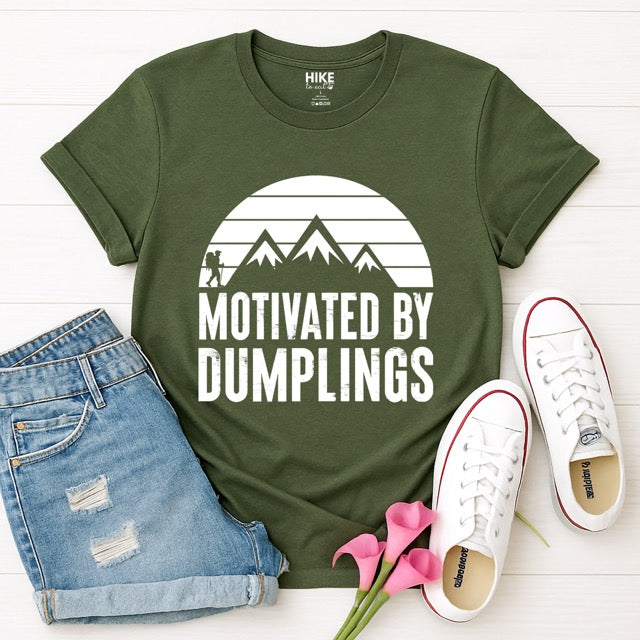 military green Motivated by Dumplings retro statement tee with sunset design, mountain peaks, and hiker silhouette for dumpling lovers, flat layed with pants and shoes