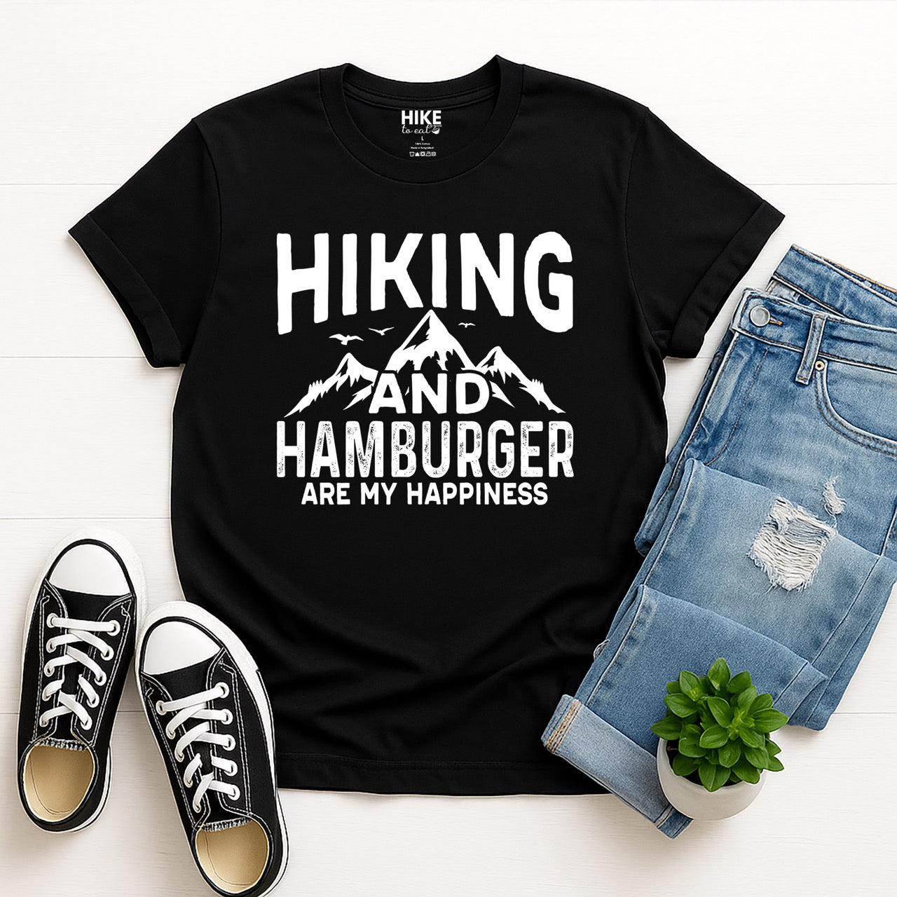 black Hiking and Hamburger are my Happiness statement tee with distressed bold typography, mountain peaks, flying birds, and pine trees for burger-loving outdoor enthusiasts and hikers - with jeans and shoes