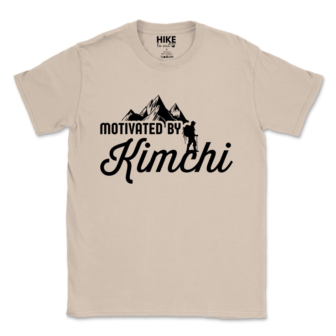 sand (beige) colored Motivated by Kimchi statement tee with bold typography, elegant script lettering, mountain peaks, and hiker silhouette for Korean food-loving outdoor enthusiasts, foodies and hikers