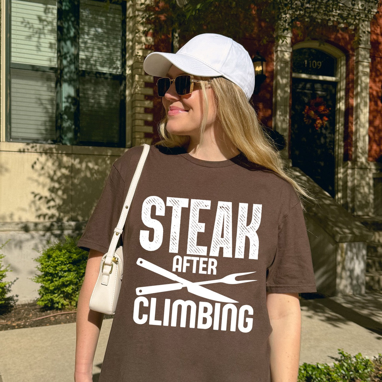 Woman wearing dark chocolate (brown) Steak after Climbing statement tee with distressed bold typography and crossed knife and fork for rock climbing and steak-loving outdoor enthusiasts, hikers and foodies