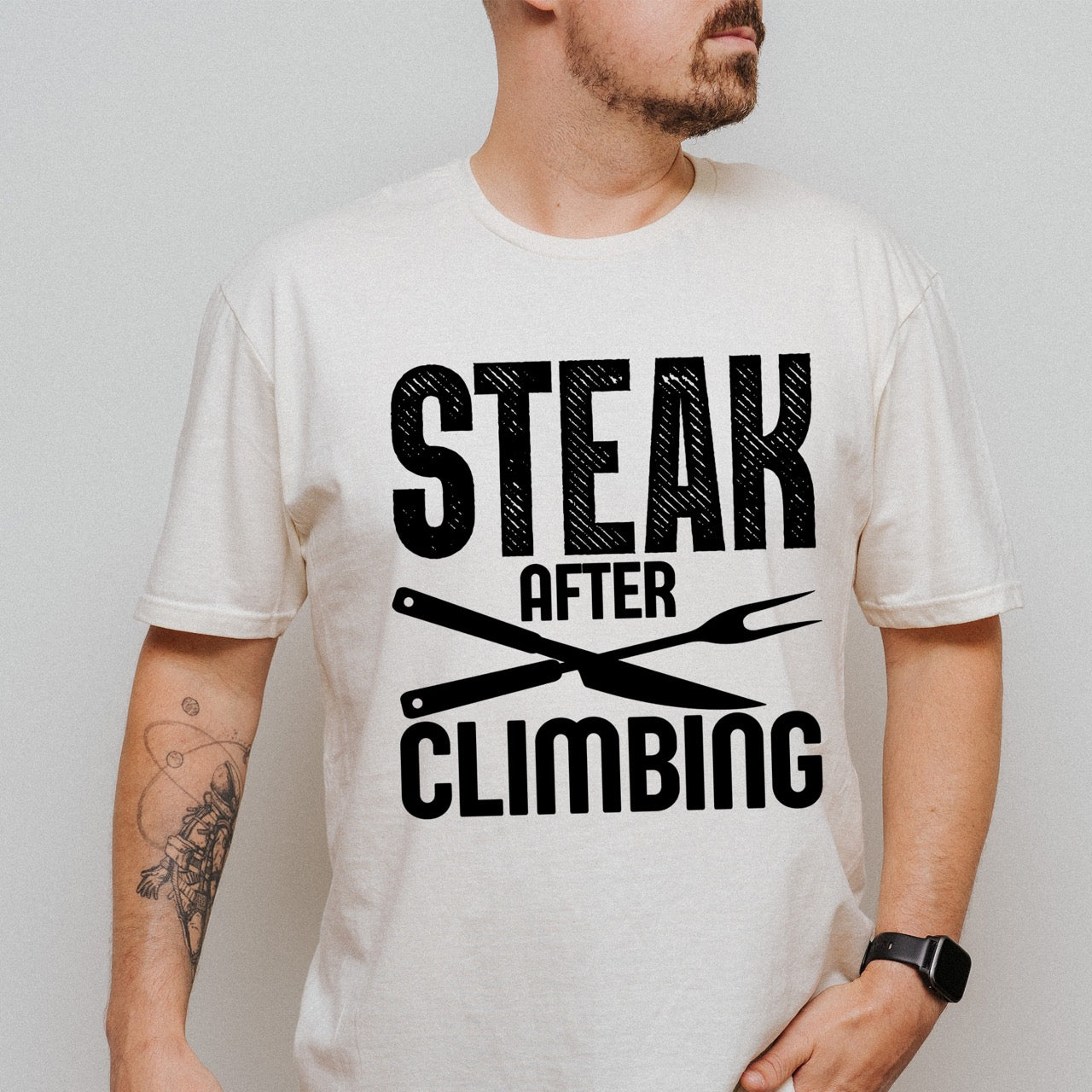 man wearing natural (beige) Steak after Climbing statement tee with distressed bold typography and crossed knife and fork for rock climbing and steak-loving outdoor enthusiasts, hikers and foodies