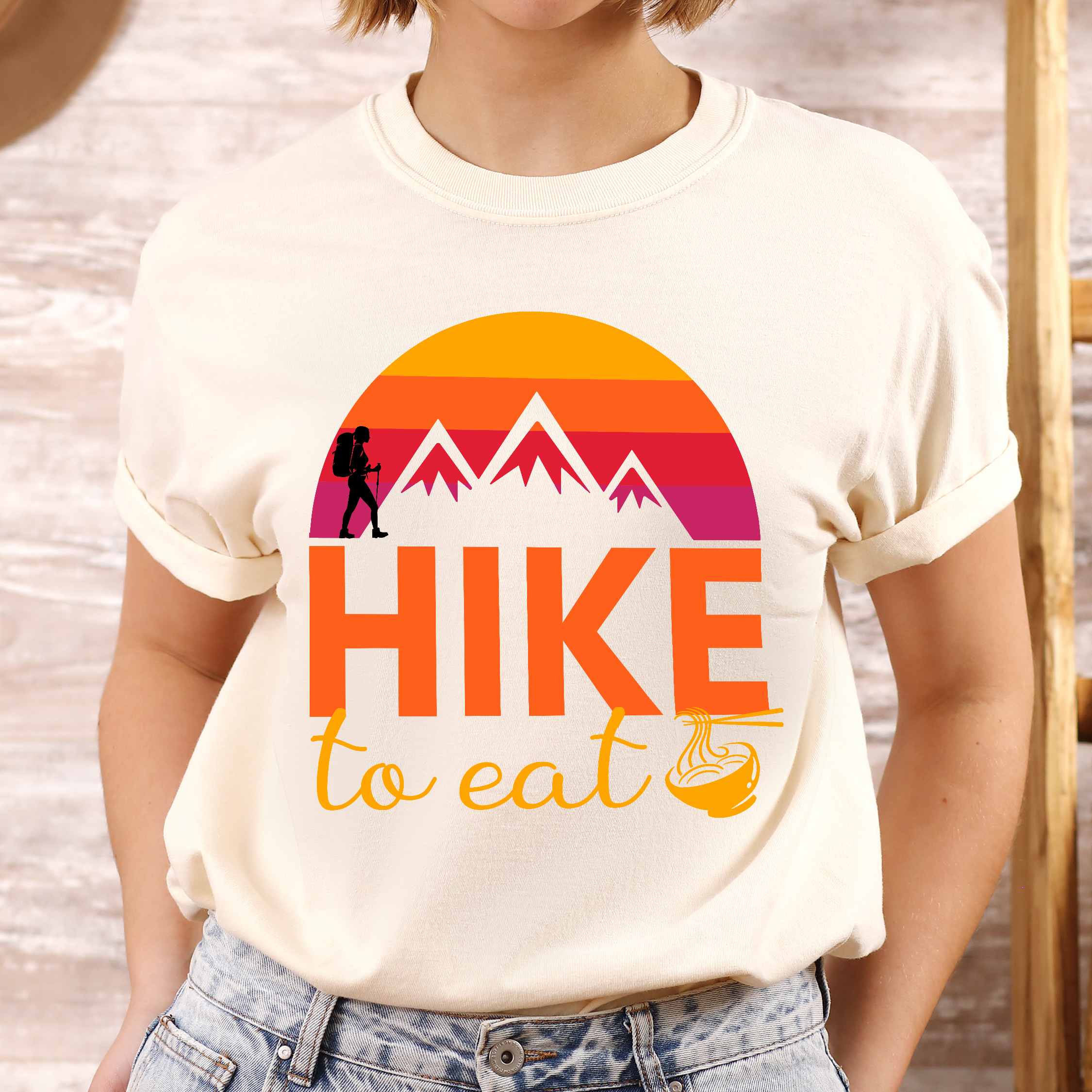 Woman wearing ivory "Hike to Eat" colored vintage tee with bold typography, mountains, sunrise, and backpacker to savor each step along the trail.