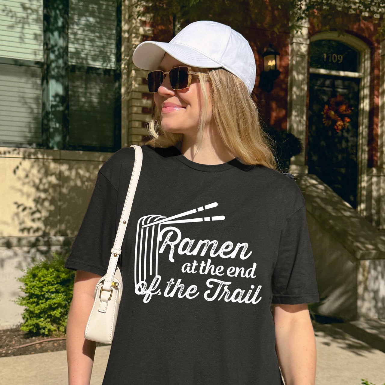woman wearing Black Ramen at the End of the Trail statement tee with elegant script typography, ramen bowl illustration, and chopsticks for Japanese noodle-loving outdoor enthusiasts, foodies and hikers