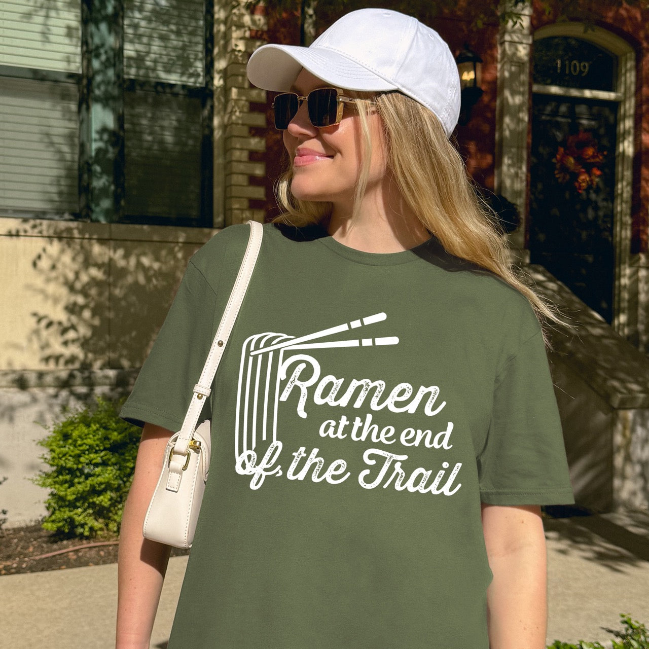 Woman wearing Military Green Ramen at the End of the Trail statement tee with elegant script typography, ramen bowl illustration, and chopsticks for Japanese noodle-loving outdoor enthusiasts, foodies and hikers
