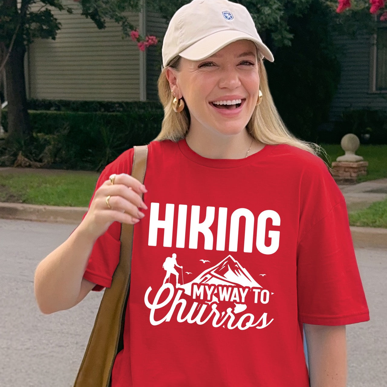 Woman smiling and wearing Red Hiking my way to Churros statement tee with bold typography, script lettering, mountain peaks, hiker silhouette, and flying birds for Spanish dessert-loving outdoor enthusiasts, hikers and foodies