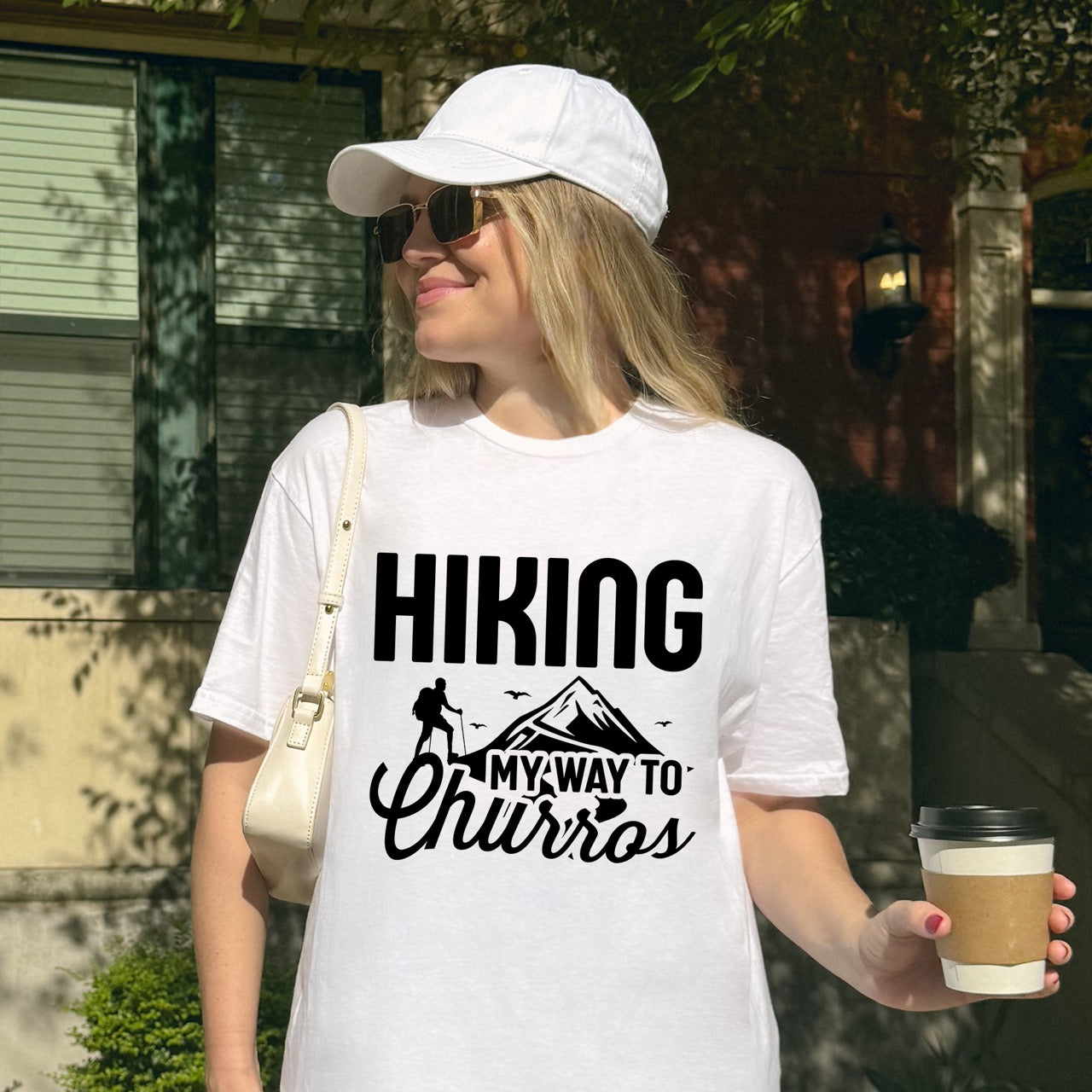 woman wearing white Hiking my way to Churros statement tee with bold typography, script lettering, mountain peaks, hiker silhouette, and flying birds for Spanish dessert-loving outdoor enthusiasts, hikers and foodies