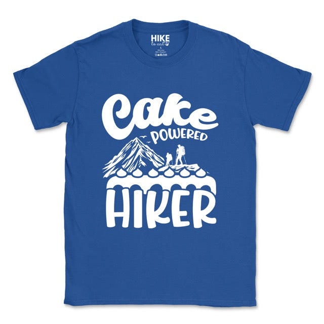 Royal Blue Cake Powered Hiker statement tee with flowing script typography, bold lettering, mountain peaks, two hiker silhouettes, flying birds, and decorative cake illustration for dessert-loving outdoor enthusiasts, hikers and foodies
