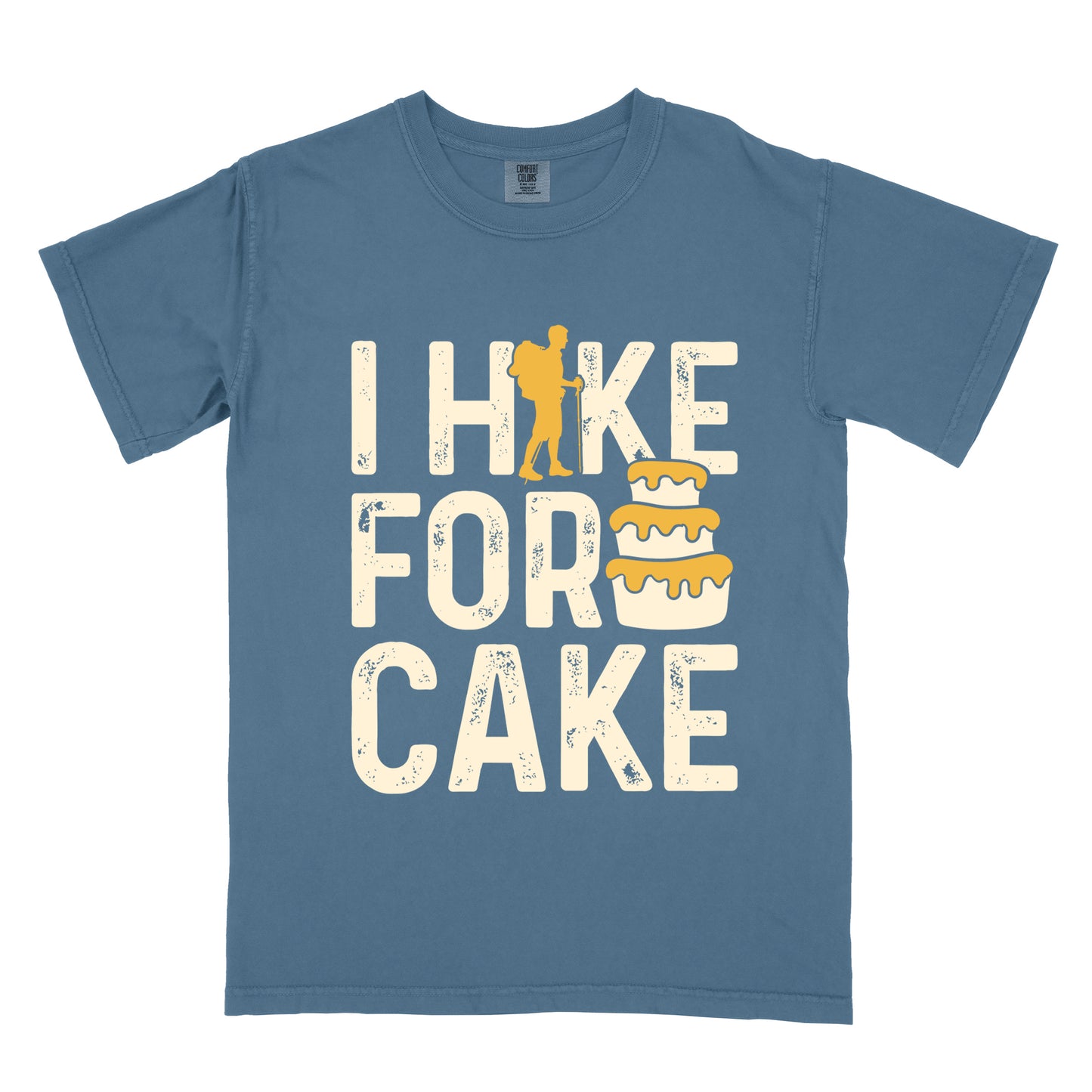 Blue Jean (Denim Blue) t-shirt with distressed cream-colored text reading "I HIKE FOR CAKE". The letter "I" in "HIKE" is replaced with a gold silhouette of a hiker with backpack and walking stick. Next to the word "FOR" is an illustration of a three-tiered cake with gold/yellow frosting dripping down the sides. All text appears in a vintage, slightly worn style against the Blue Jean (Denim Blue) shirt background.